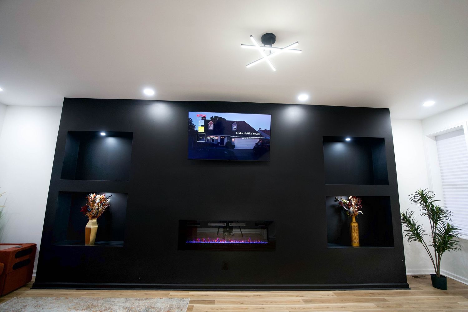 Modern living room featuring a black accent wall with built-in shelves, electric fireplace, and wall-mounted TV with LED lighting.