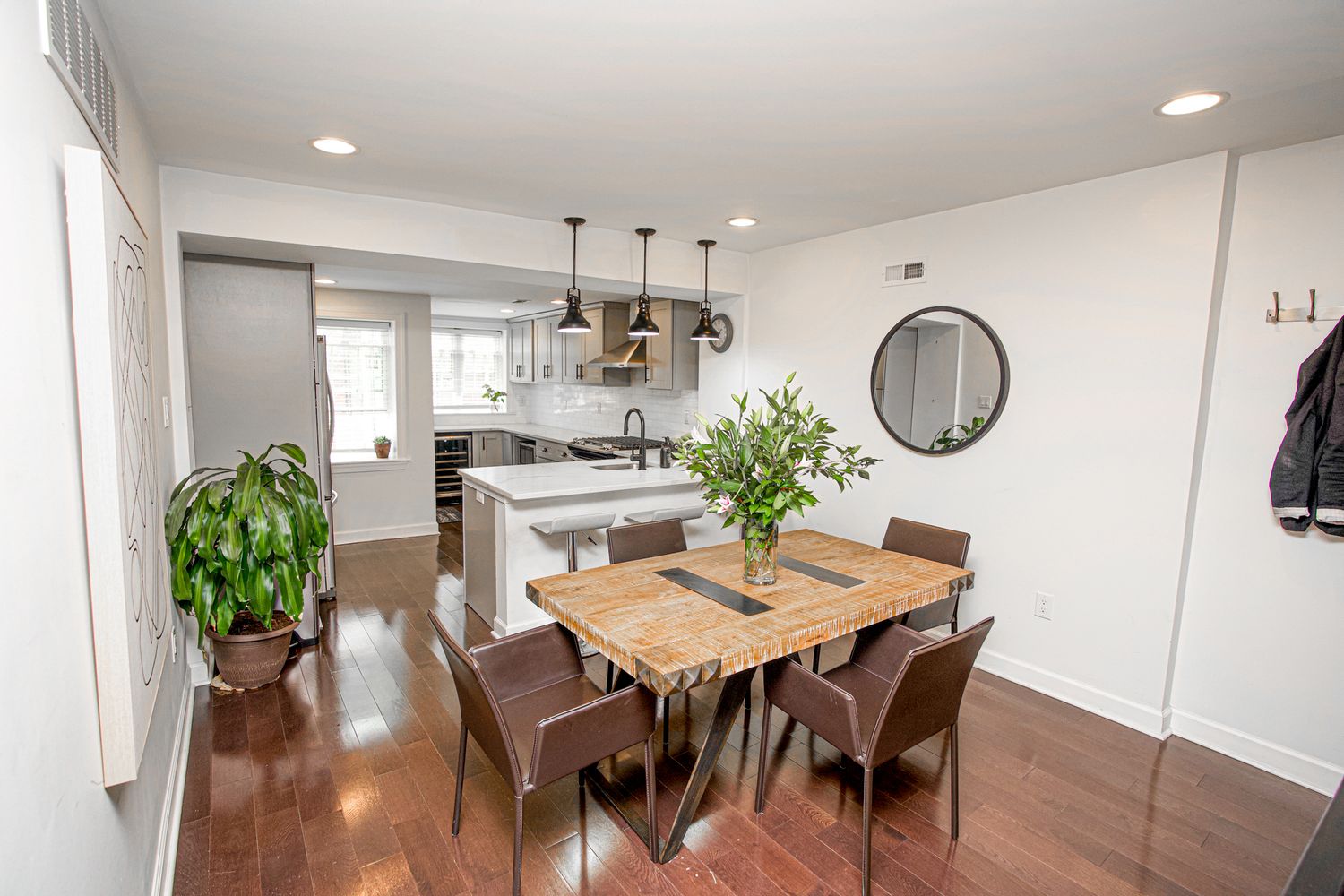 Modern open-plan dining area with wooden table, brown chairs, and kitchen visible in background.