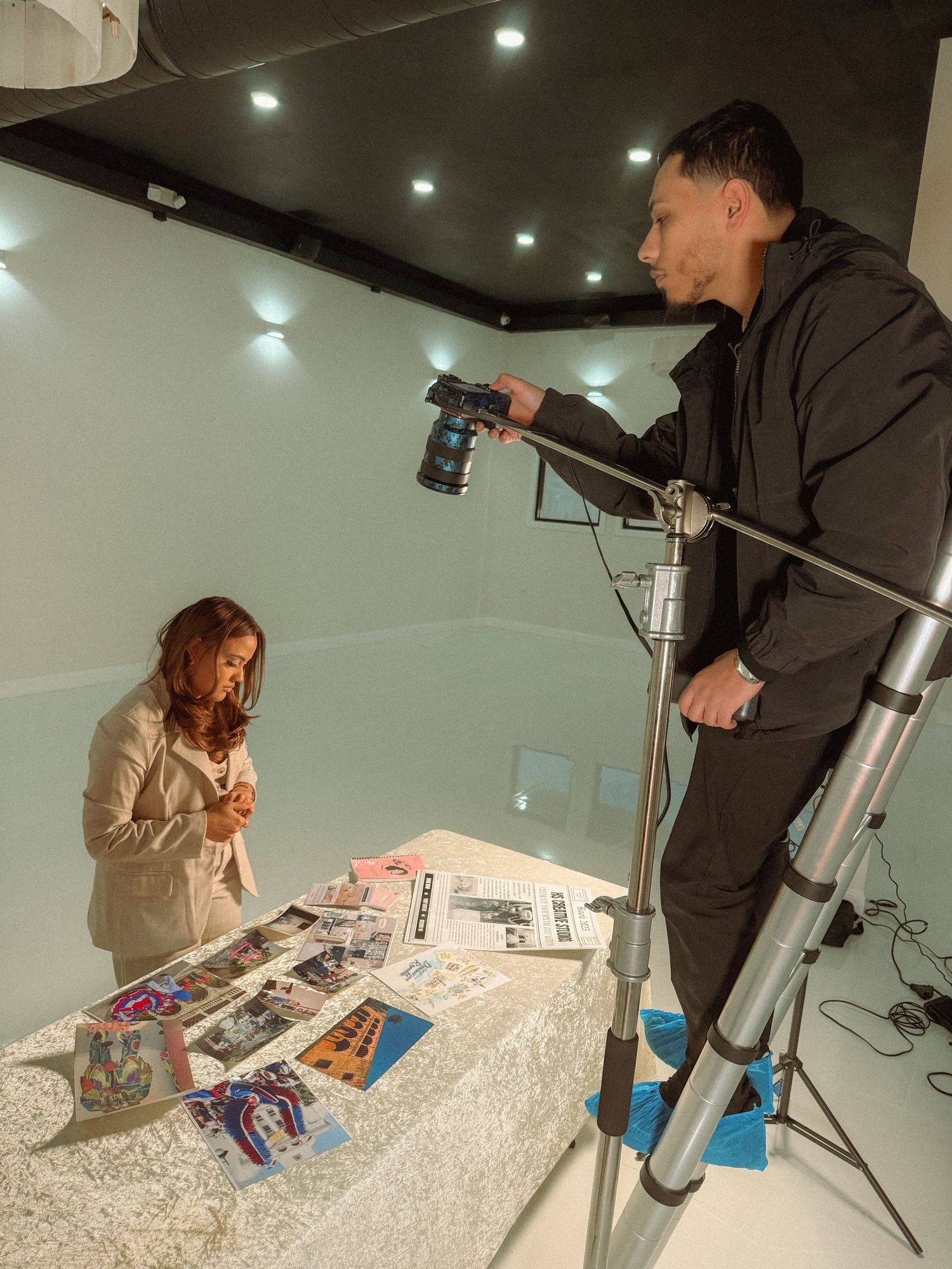 Photographer on ladder capturing product shots on white table in studio setting.