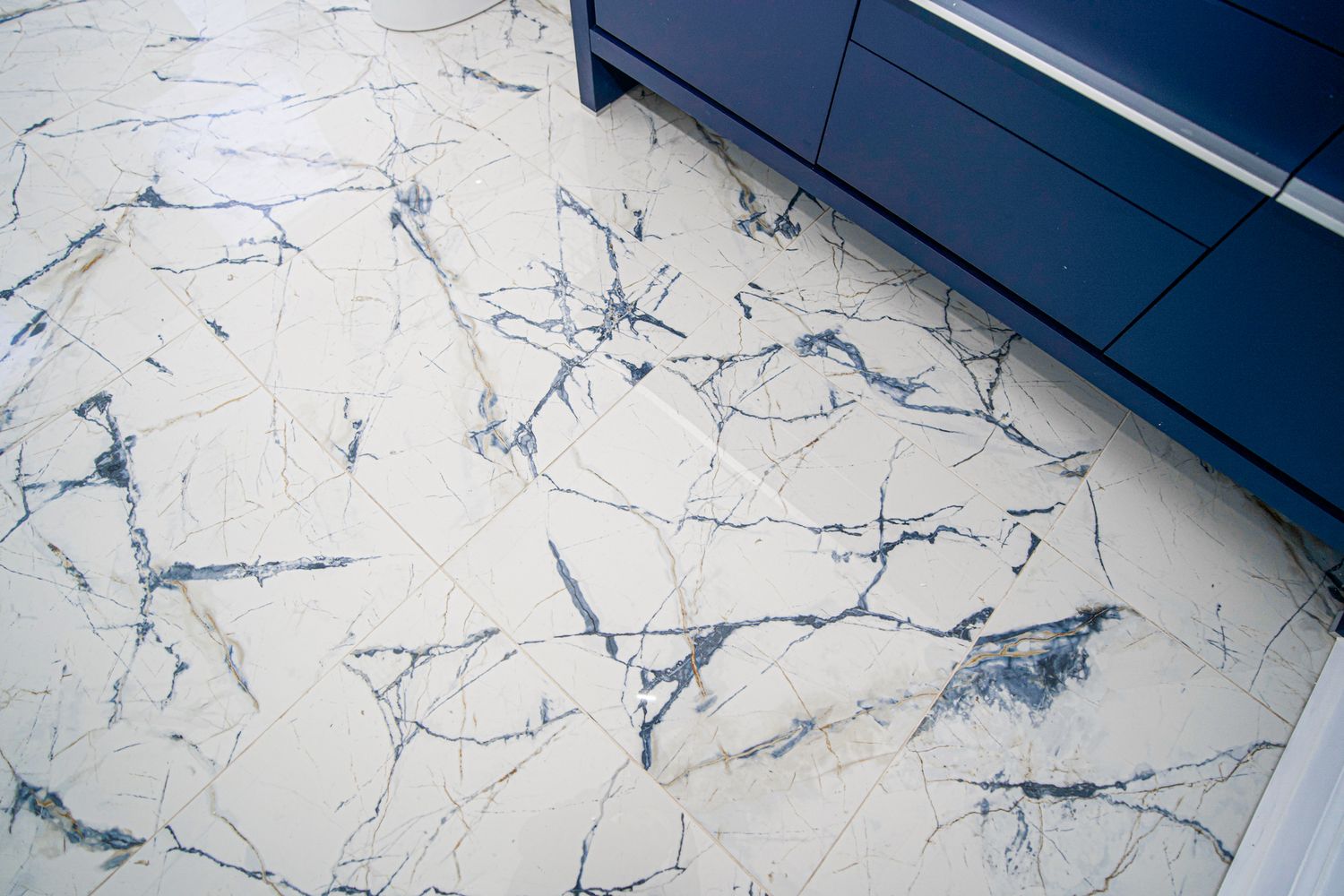 Luxurious white marble floor tiles with blue veining next to a navy blue bathroom vanity.
