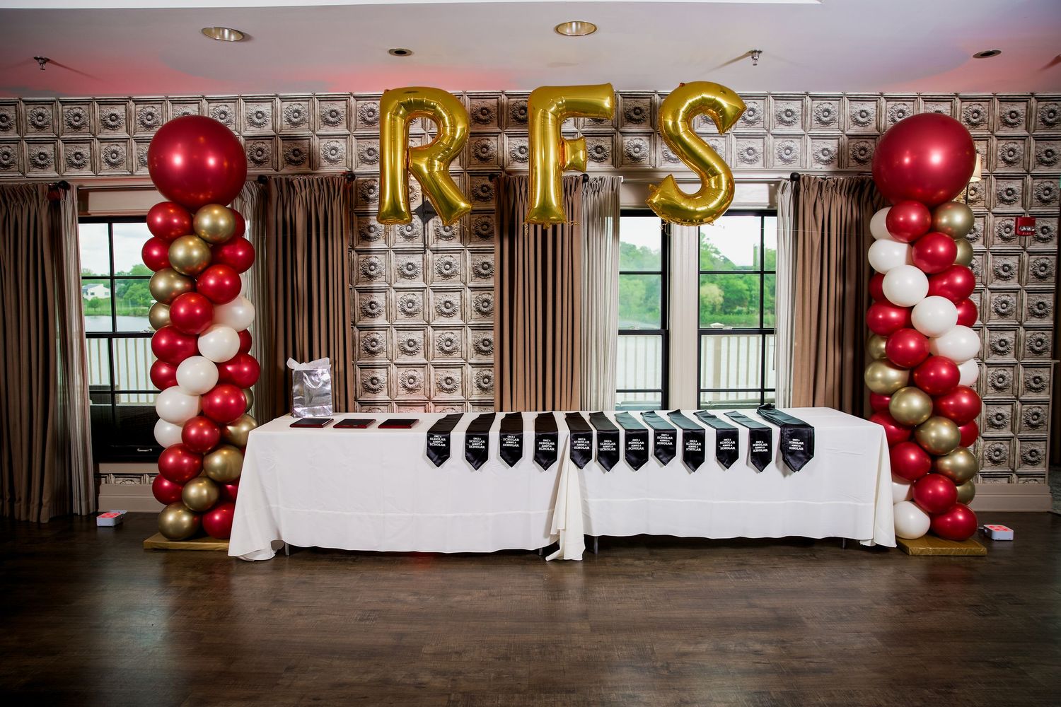 Red, white, and gold balloon columns flank a decorated table with RFS gold letter balloons at an elegant event.
