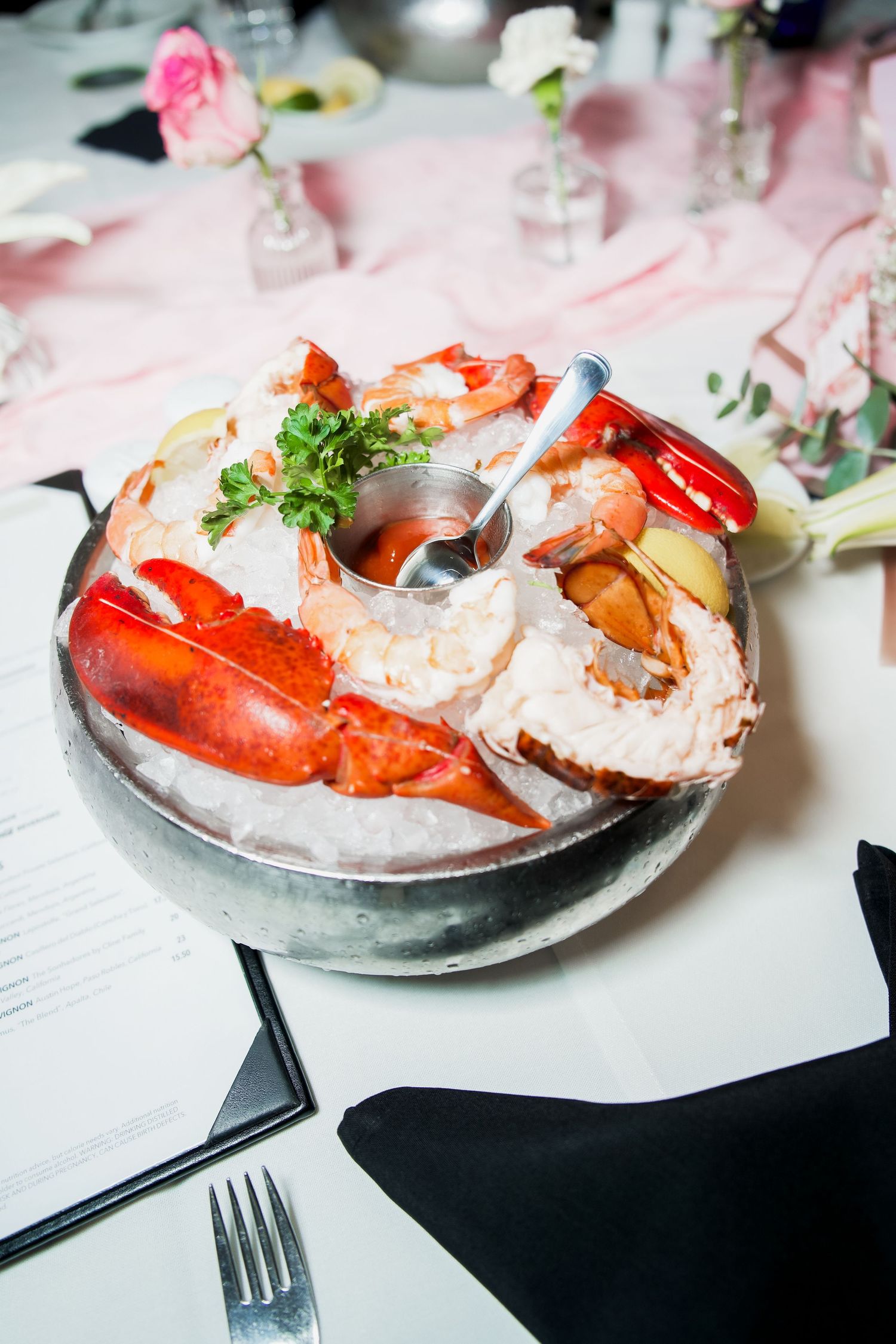 Elegant seafood platter on ice with lobster claws, shrimp, and cocktail sauce at a formal dining event.