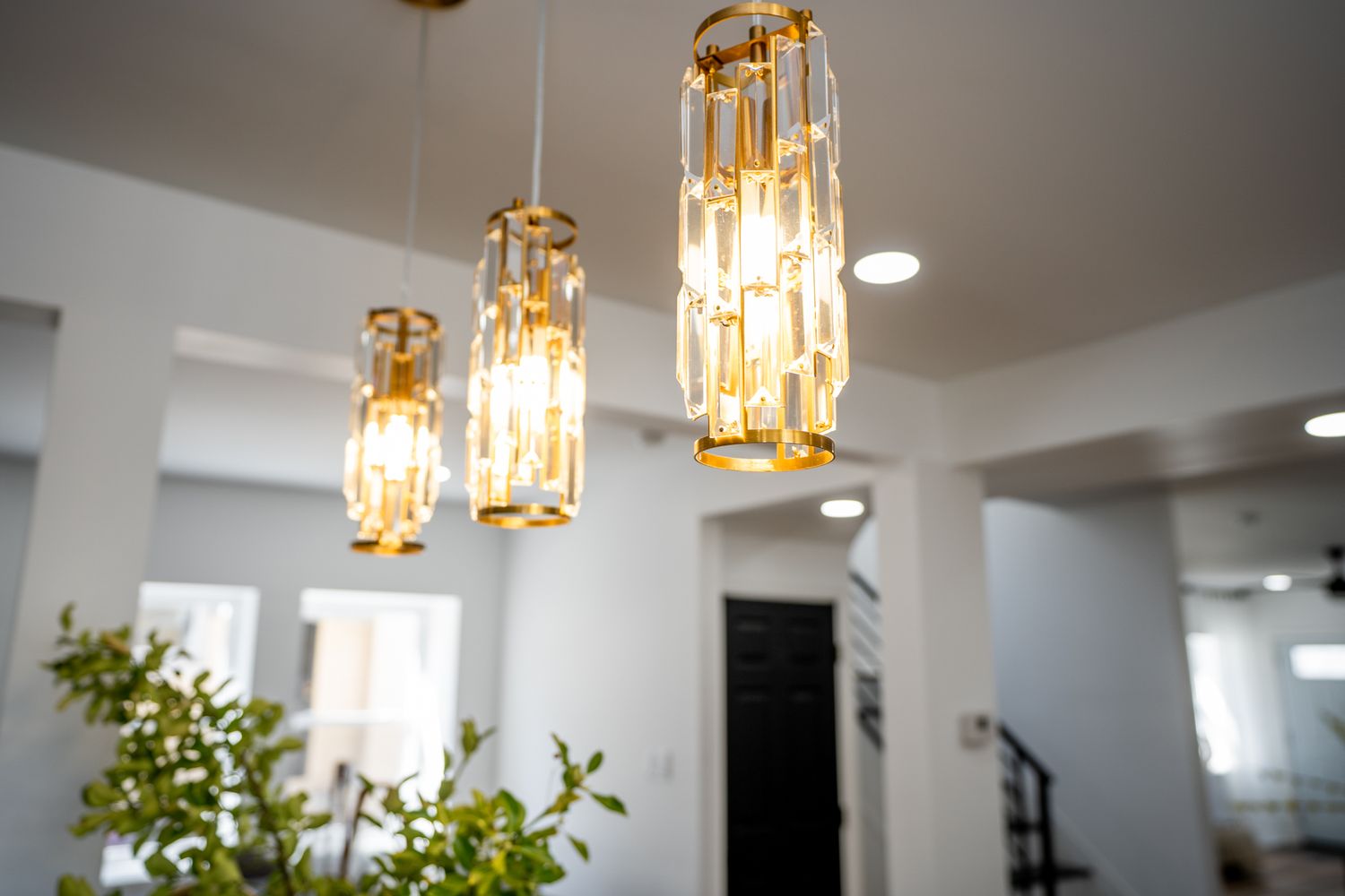 Three elegant gold crystal pendant chandeliers hanging from a white ceiling in a modern bright interior space.