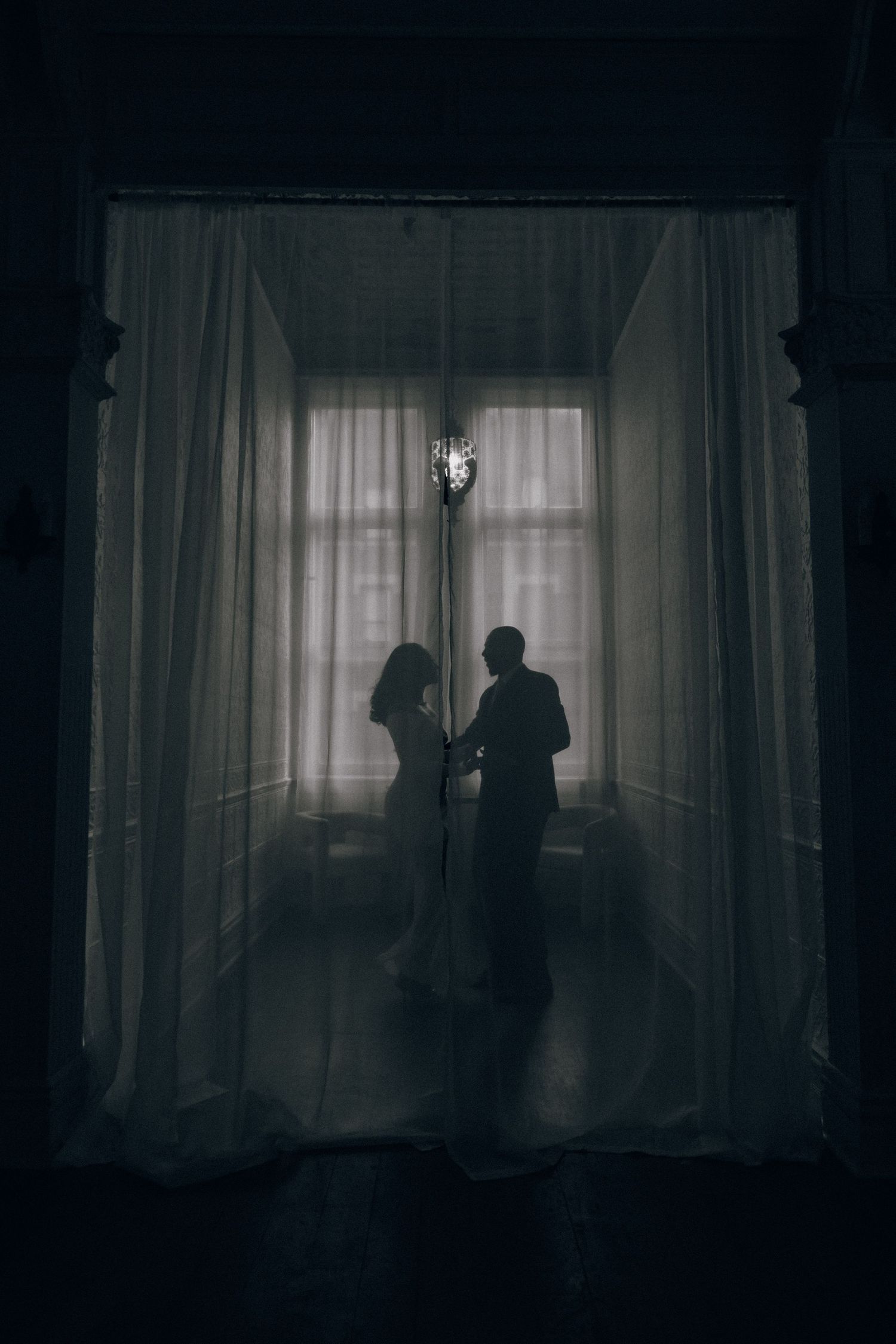 Dark silhouettes stand against curtained windows in a moody sequence of noir-style interior shots.
