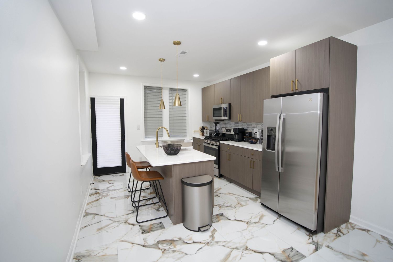 Modern kitchen with marble floors, gray cabinets, stainless steel appliances, island with bar stools, and pendant lighting.