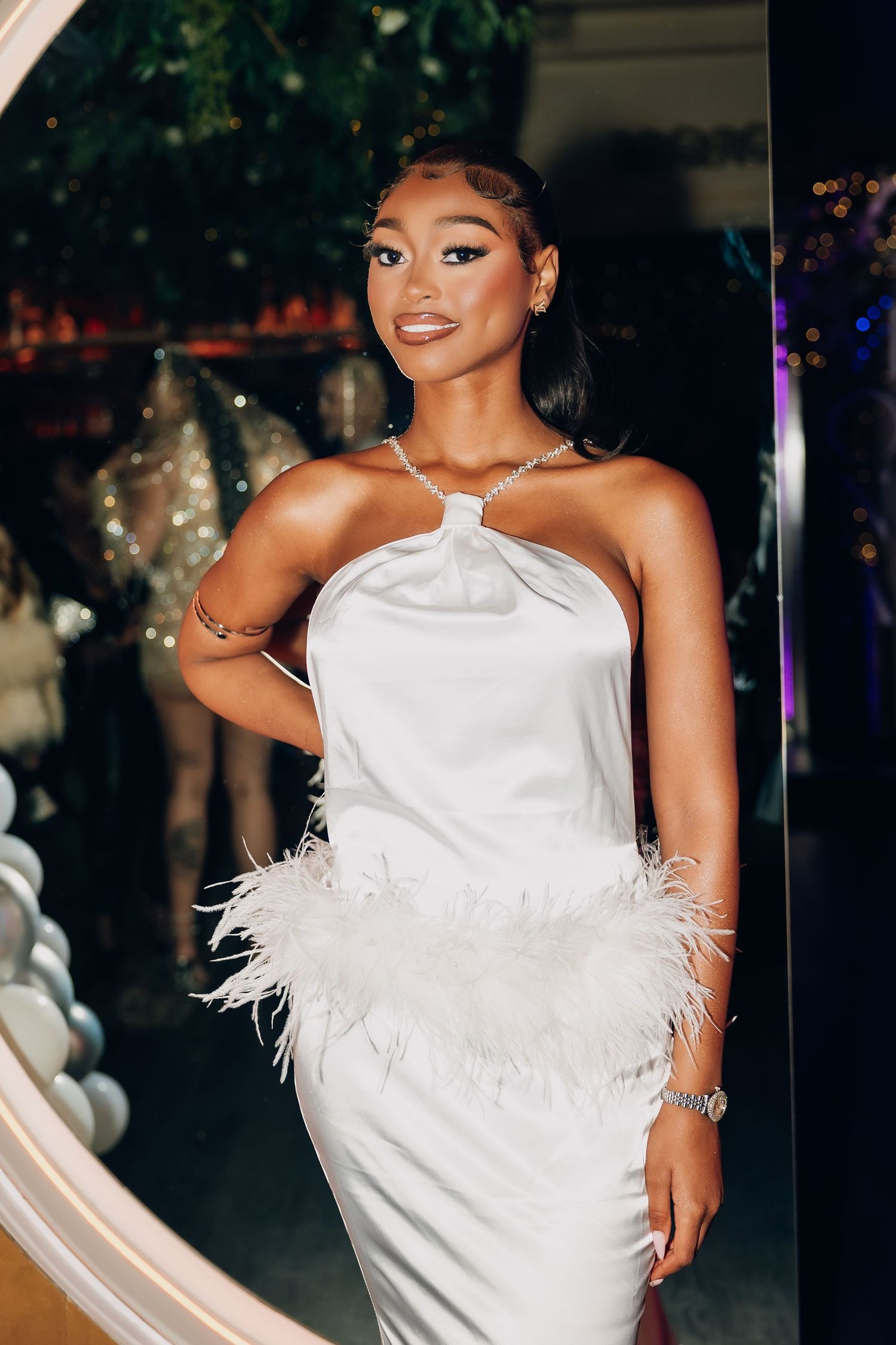 A bride poses in a glamorous white halter dress adorned with feathers and crystal details.