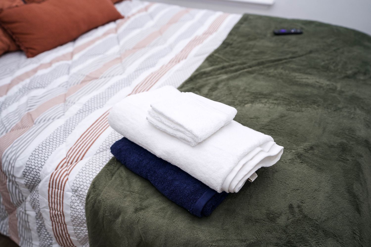 Folded white and navy towels stacked on a green bedspread in a cozy bedroom.