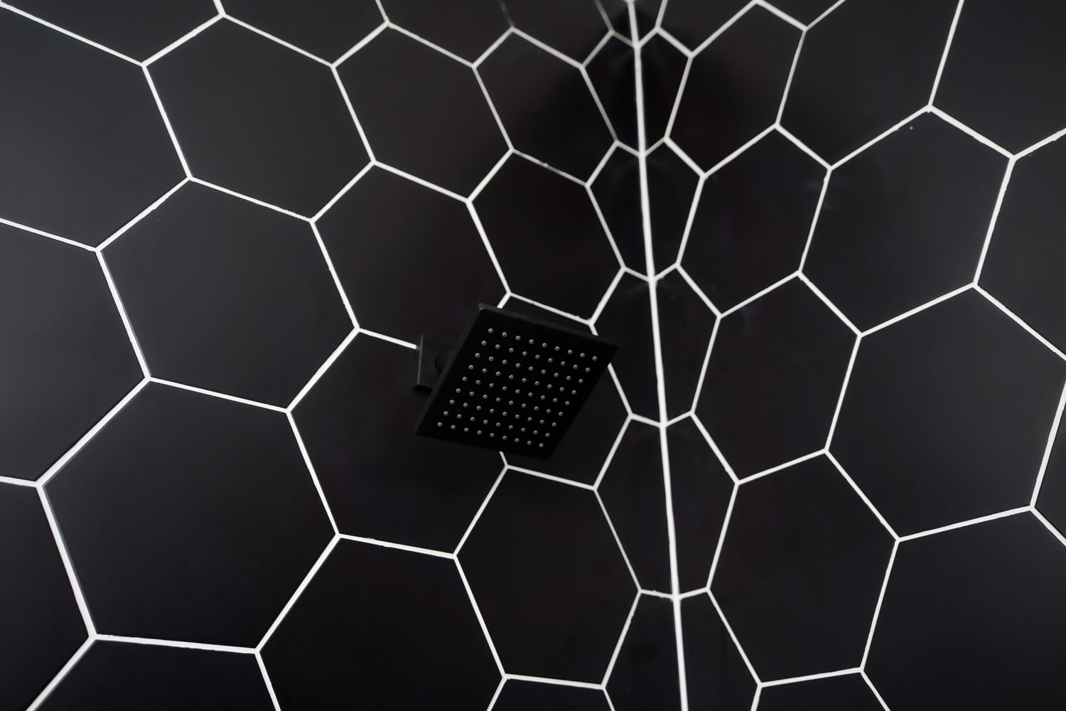 Close-up of black hexagonal shower wall tiles with white grout and a square rain shower head.