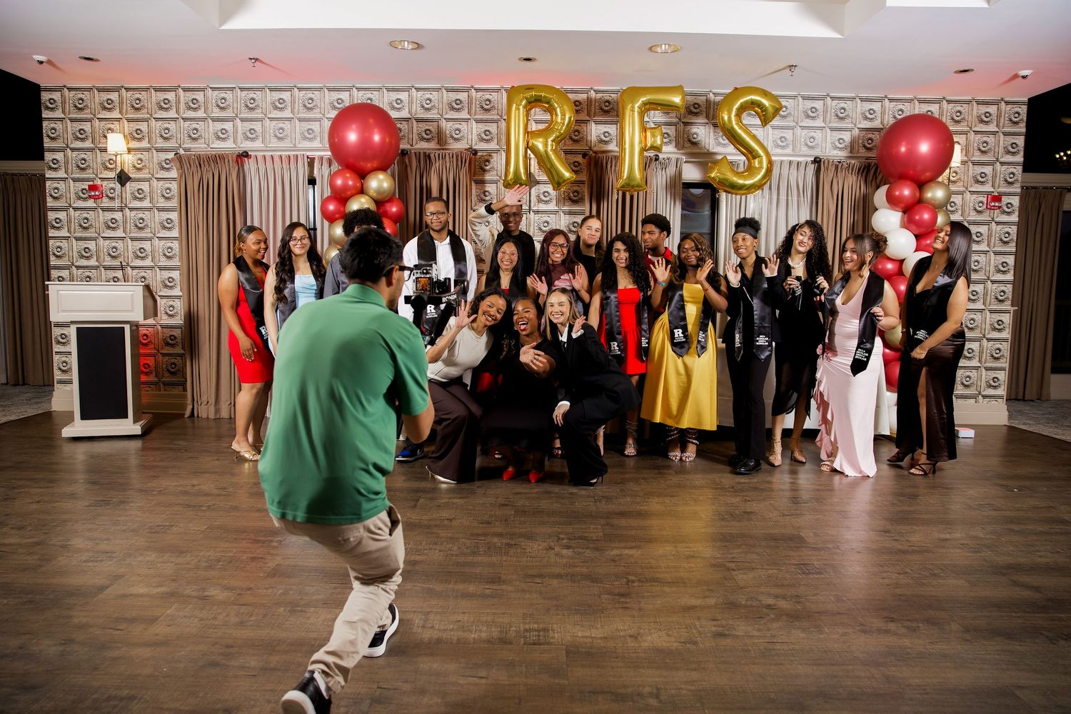 Group photo at RFS celebration event with gold letter balloons, red and gold decor, and guests posing in formal attire.