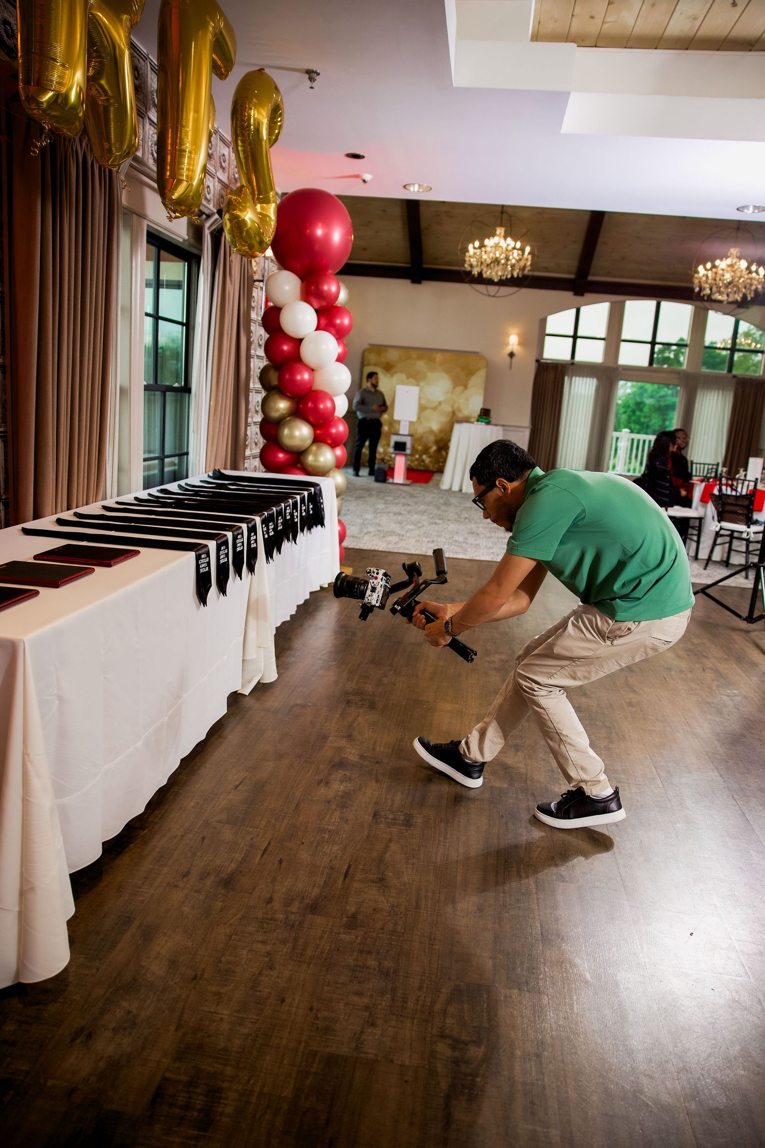 Photographer crouching to capture event setup with red and white balloon column and display table in elegant venue.