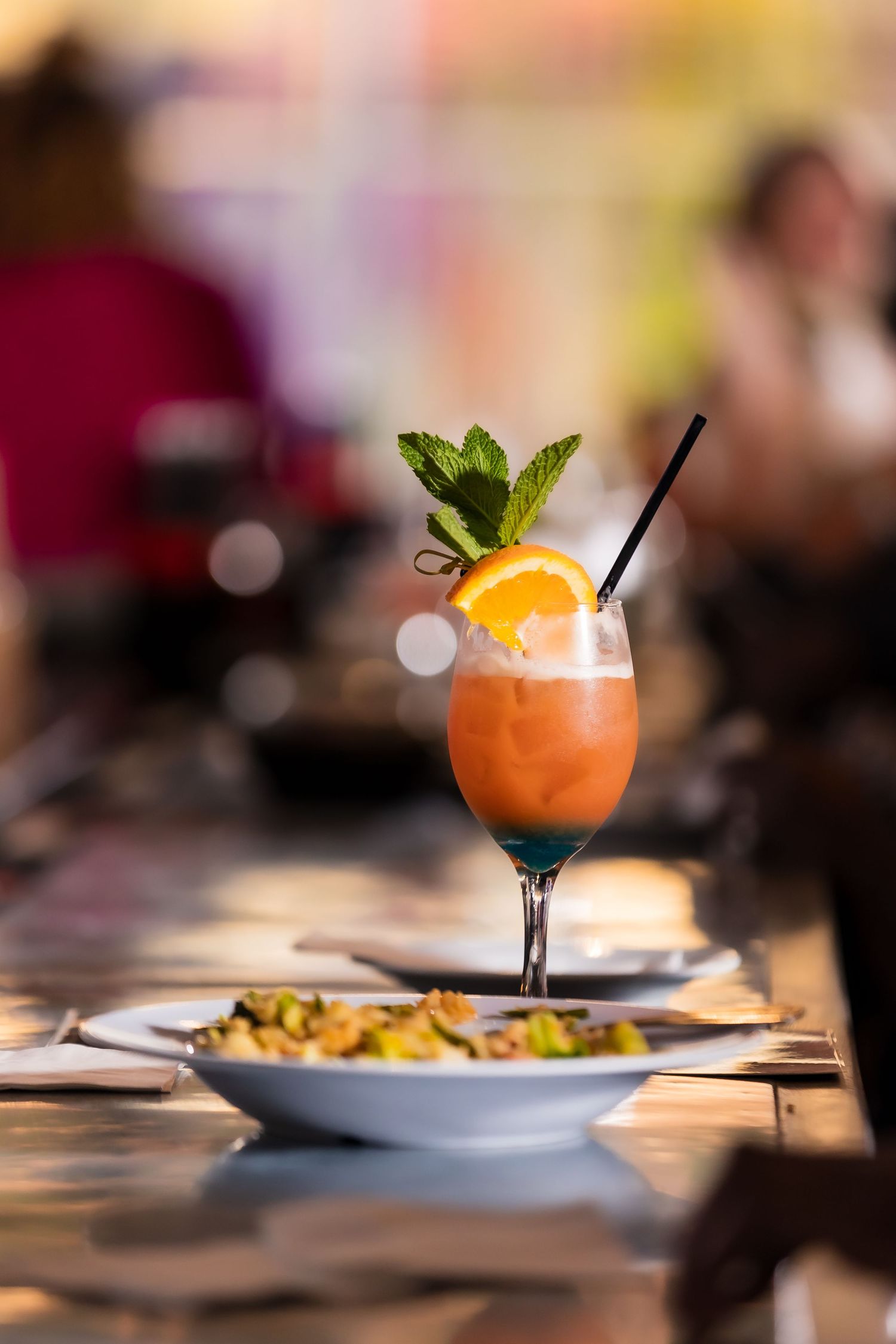 A vibrant tropical cocktail garnished with orange slice and mint, served in a stemmed glass at a restaurant table.