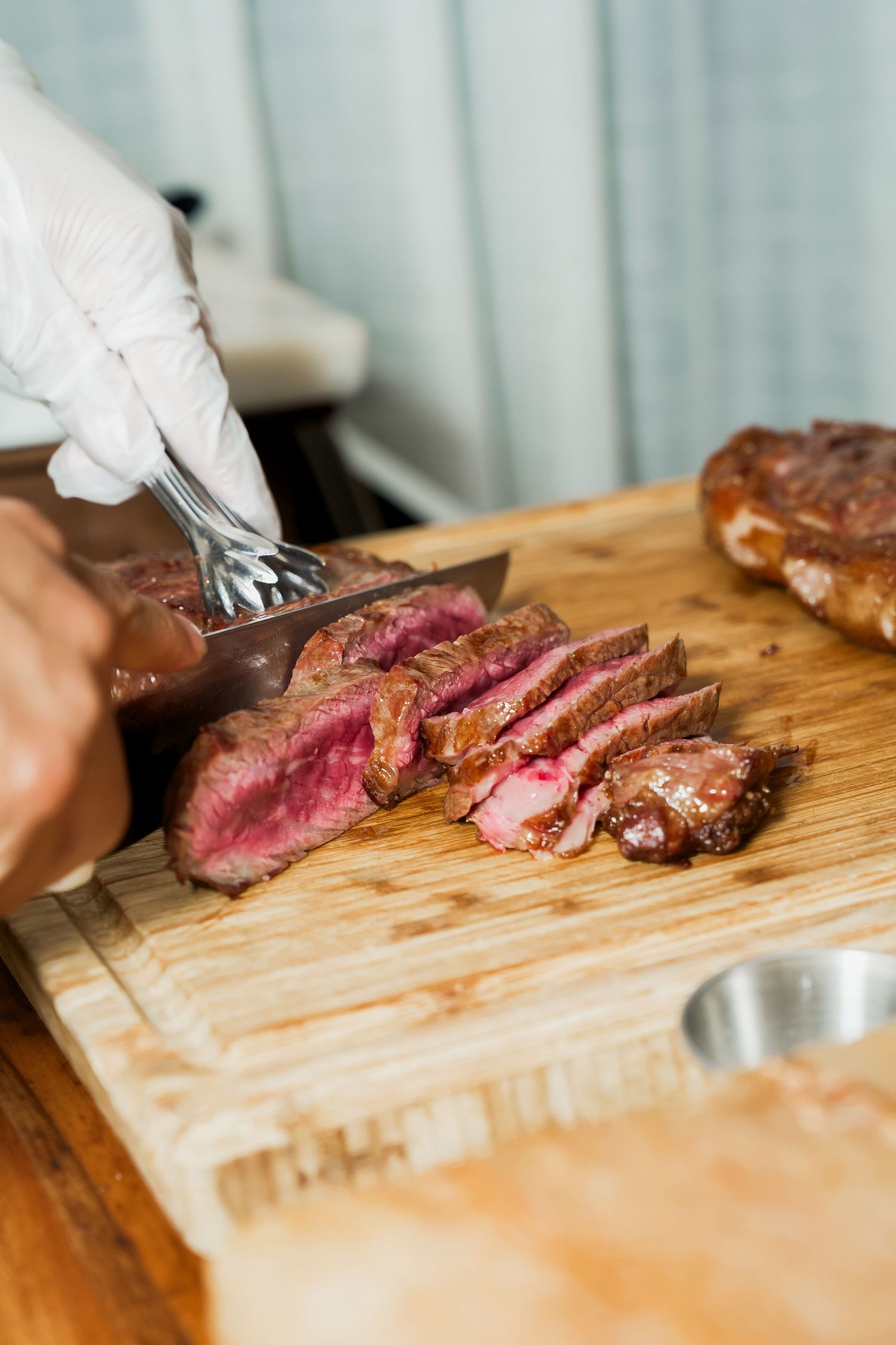 Chef in white gloves slicing a perfectly cooked medium-rare steak on a wooden cutting board.