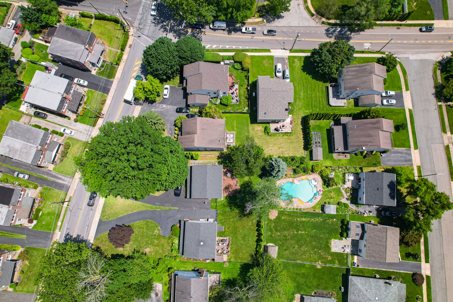 Aerial view of a suburban neighborhood with tree-lined streets, green lawns, and a backyard swimming pool.