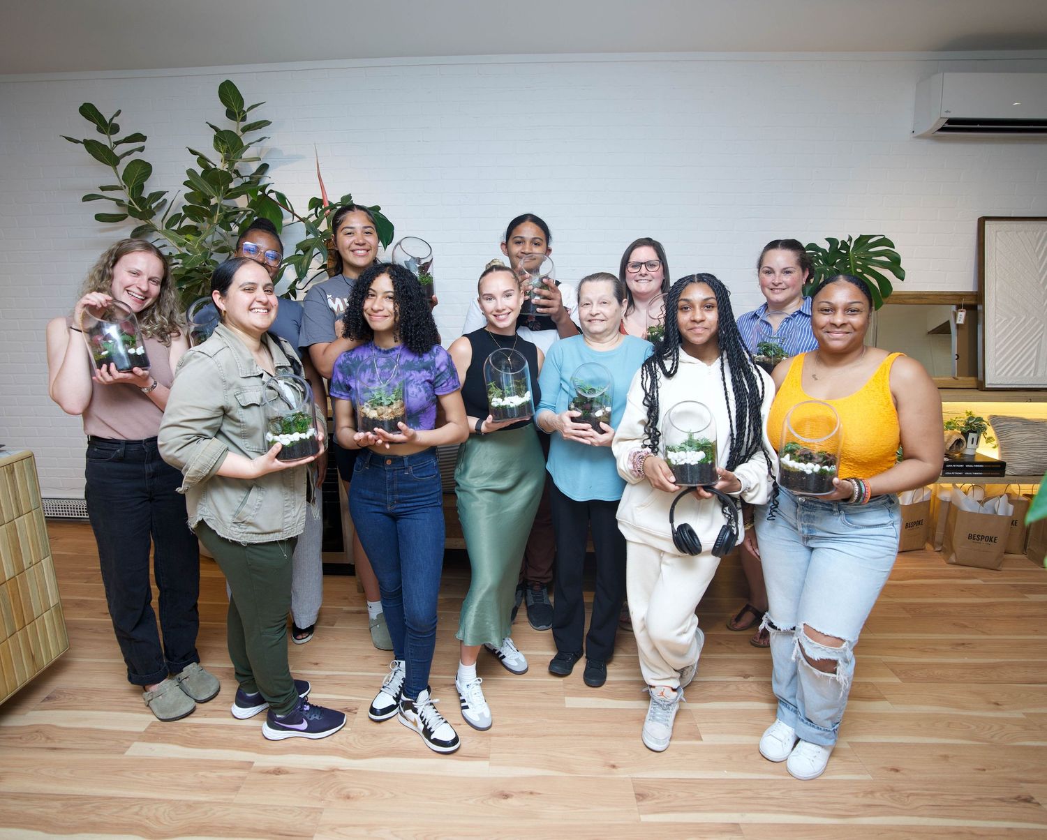 Group of women smiling and holding terrariums at a plant workshop in a bright modern studio space.