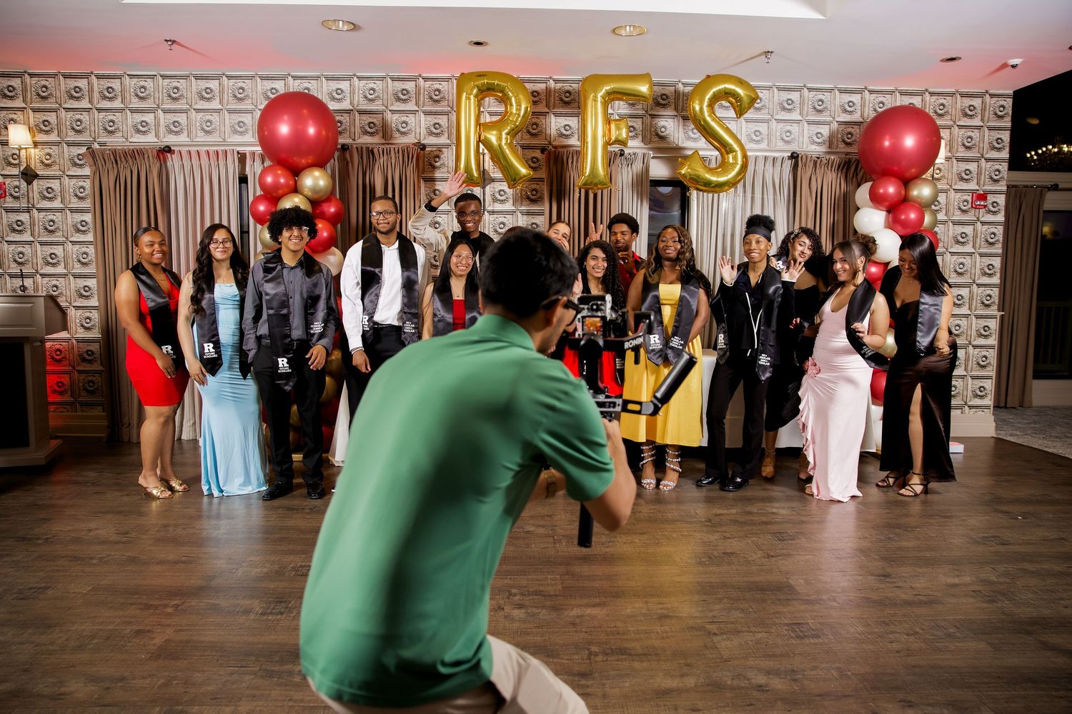 Photographer captures group photo at RFS celebration event with red and gold balloons in decorated venue.