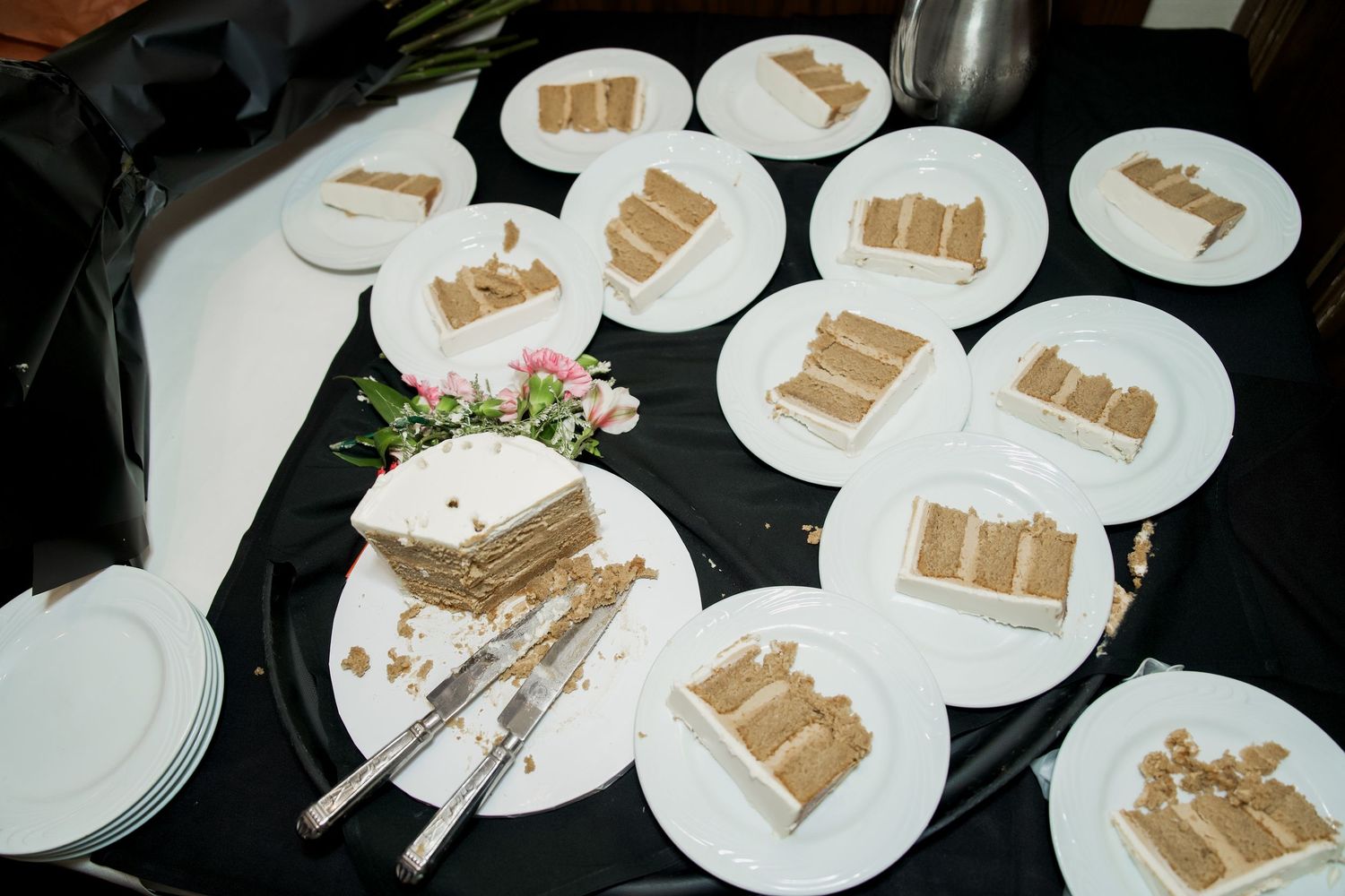 Sliced layered cake with white frosting served on white plates atop a black tablecloth at a catered event.