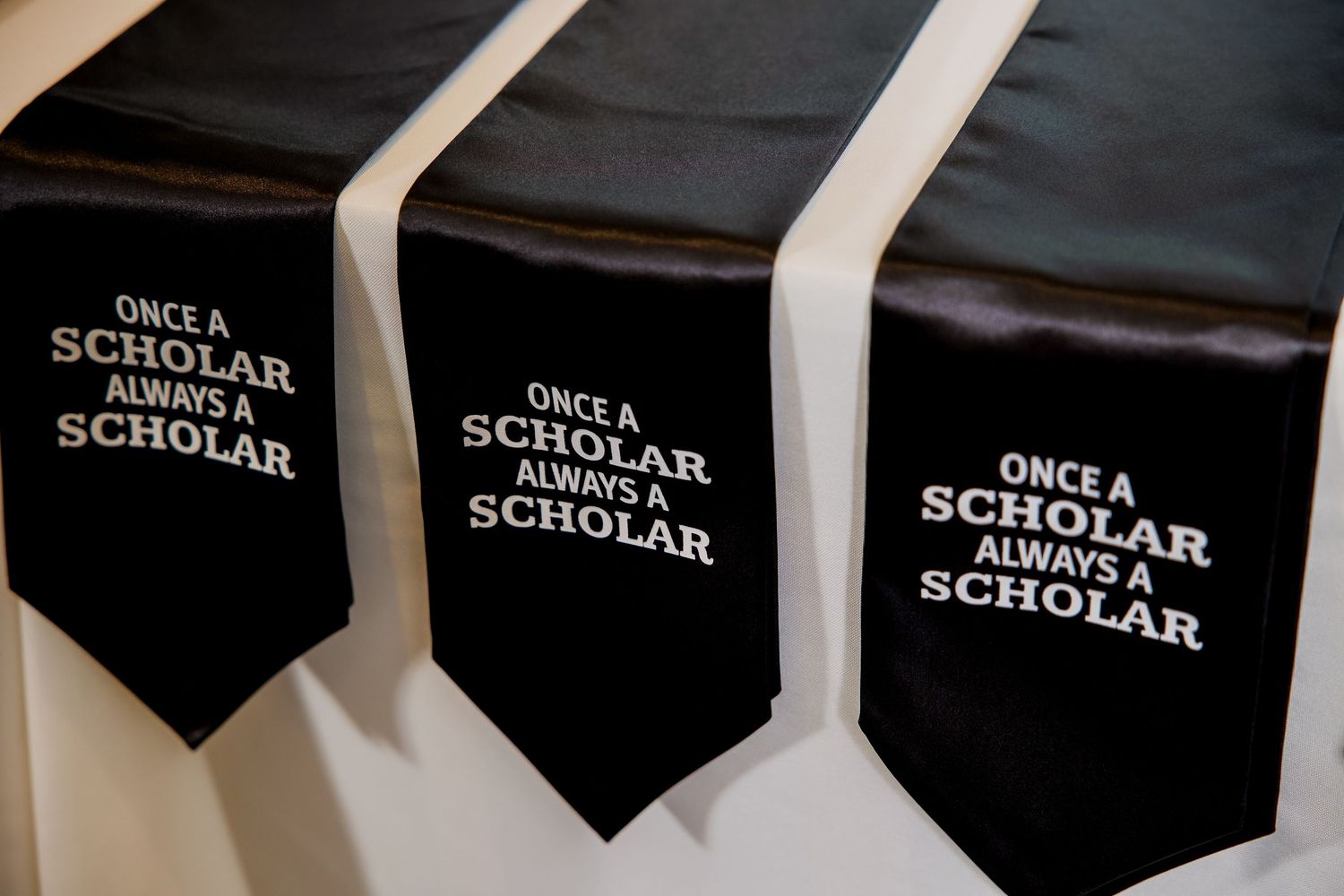 Three black pennants with white text reading Once a Scholar Always a Scholar displayed on a wall.