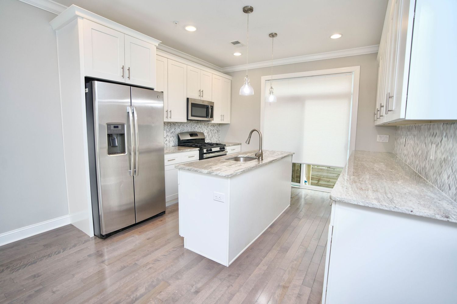 Modern kitchen with white cabinets, stainless steel appliances, granite island, and light hardwood floors.