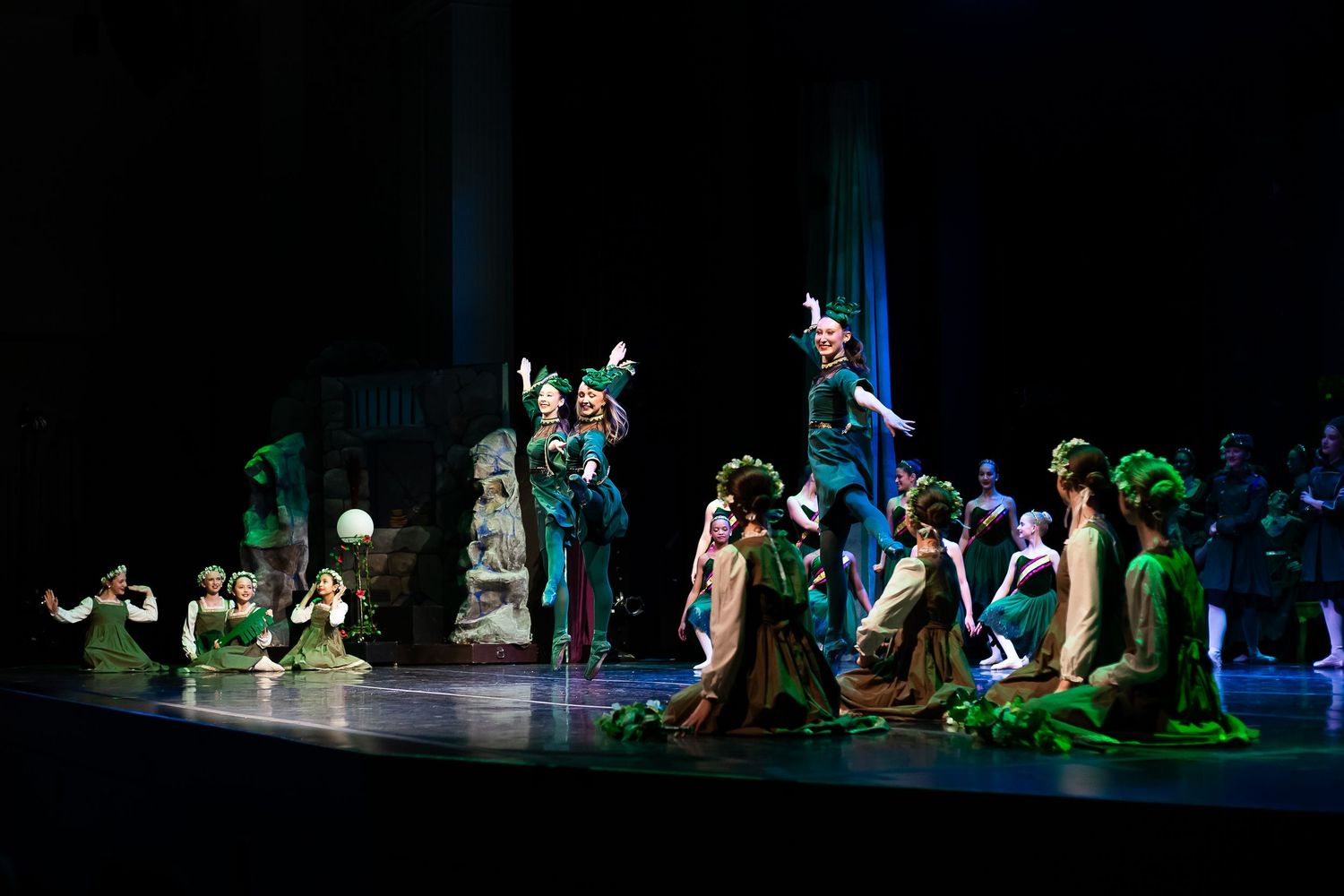 Performers in green costumes on stage during a theatrical production resembling a Peter Pan fantasy scene.