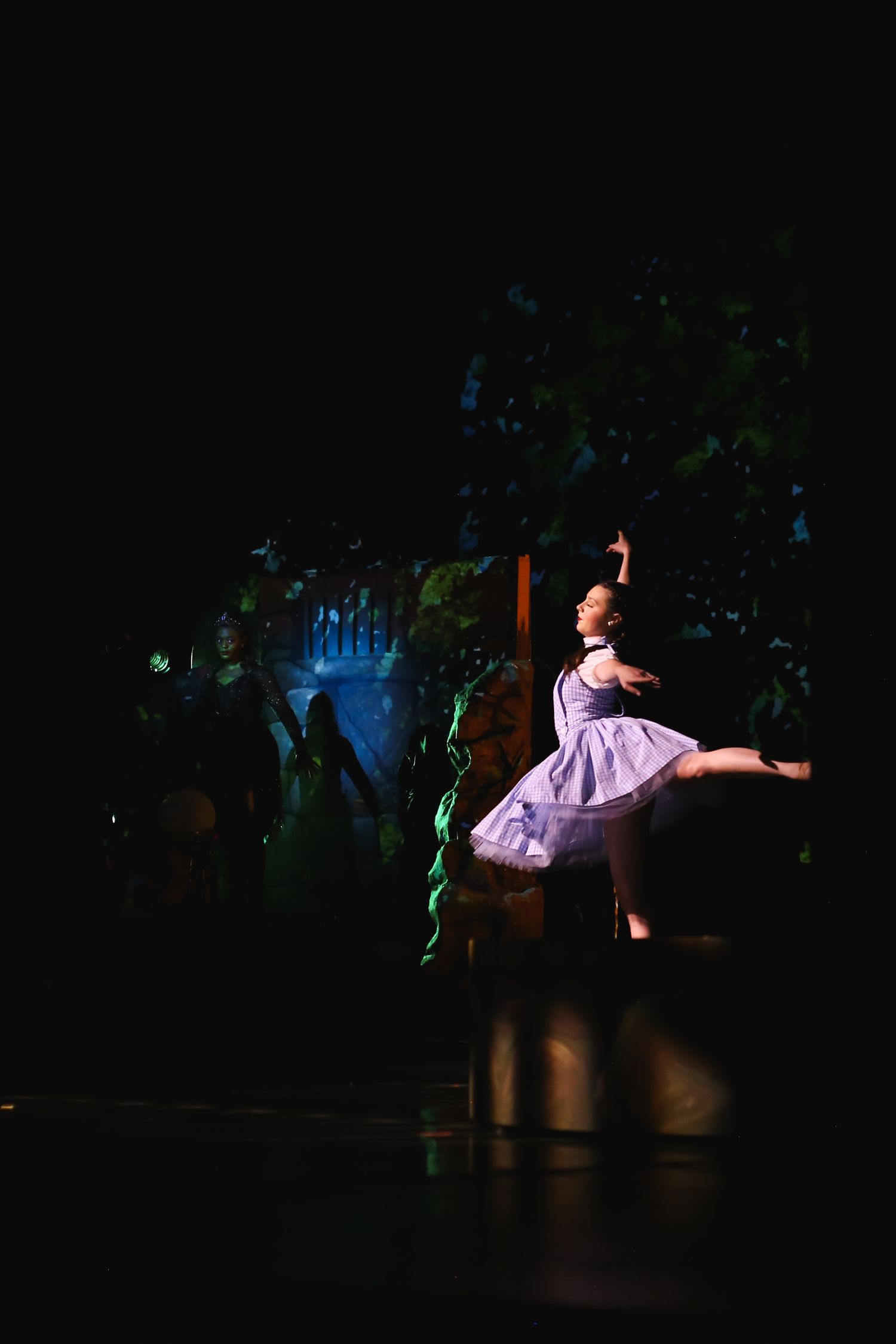 A ballerina in a white dress performs on a dimly lit stage with green scenic backdrop.