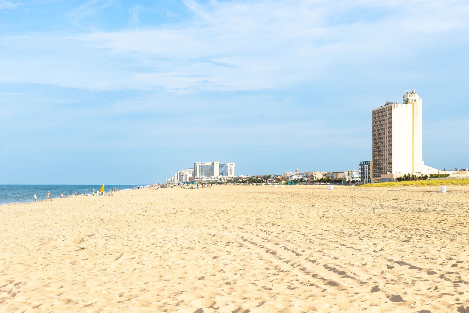 Sandy beach with calm waves, high-rise hotels, and a clear blue sky along a scenic coastal city shoreline.