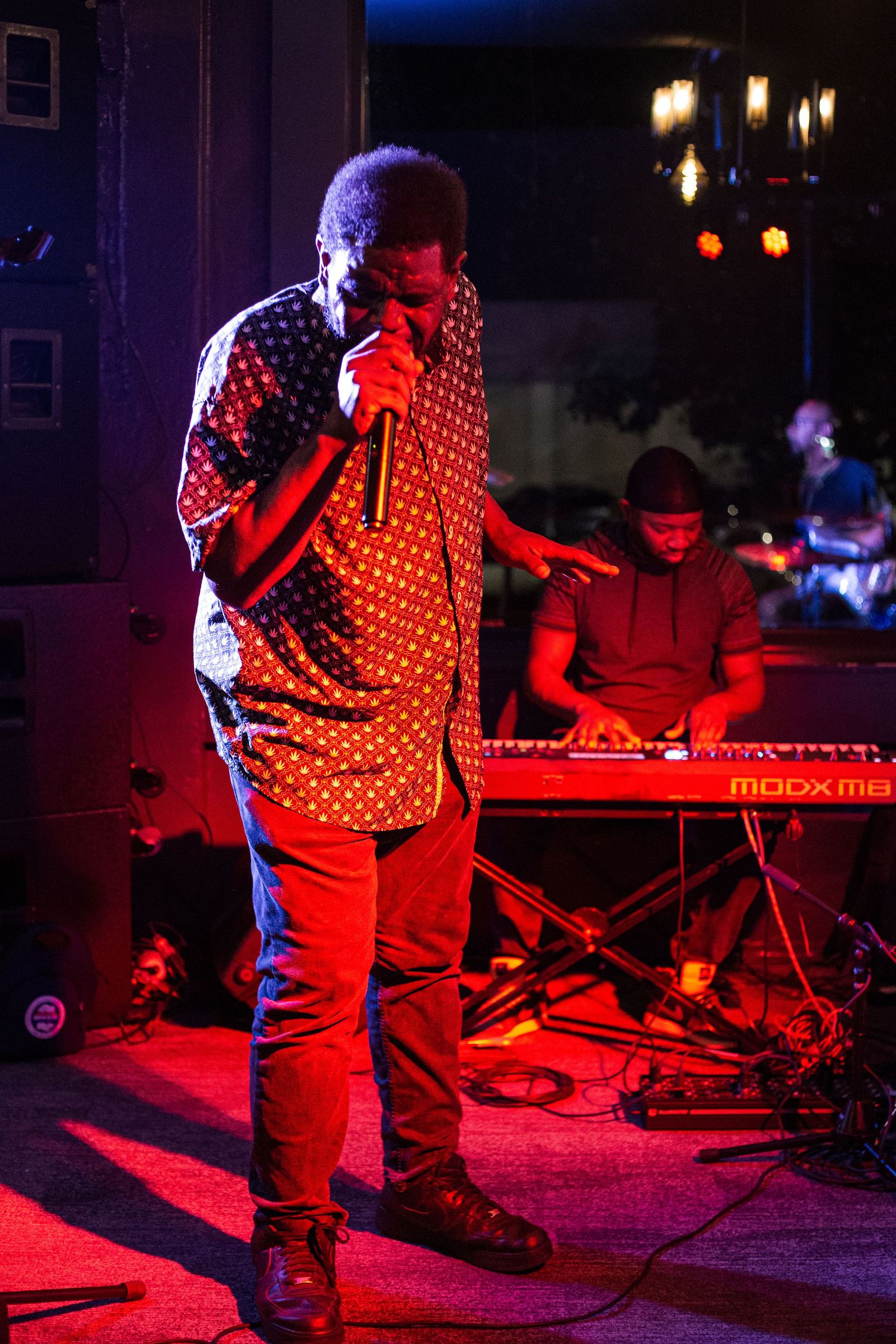 A vocalist performs on stage under red lights while a keyboardist plays a red synthesizer in the background.