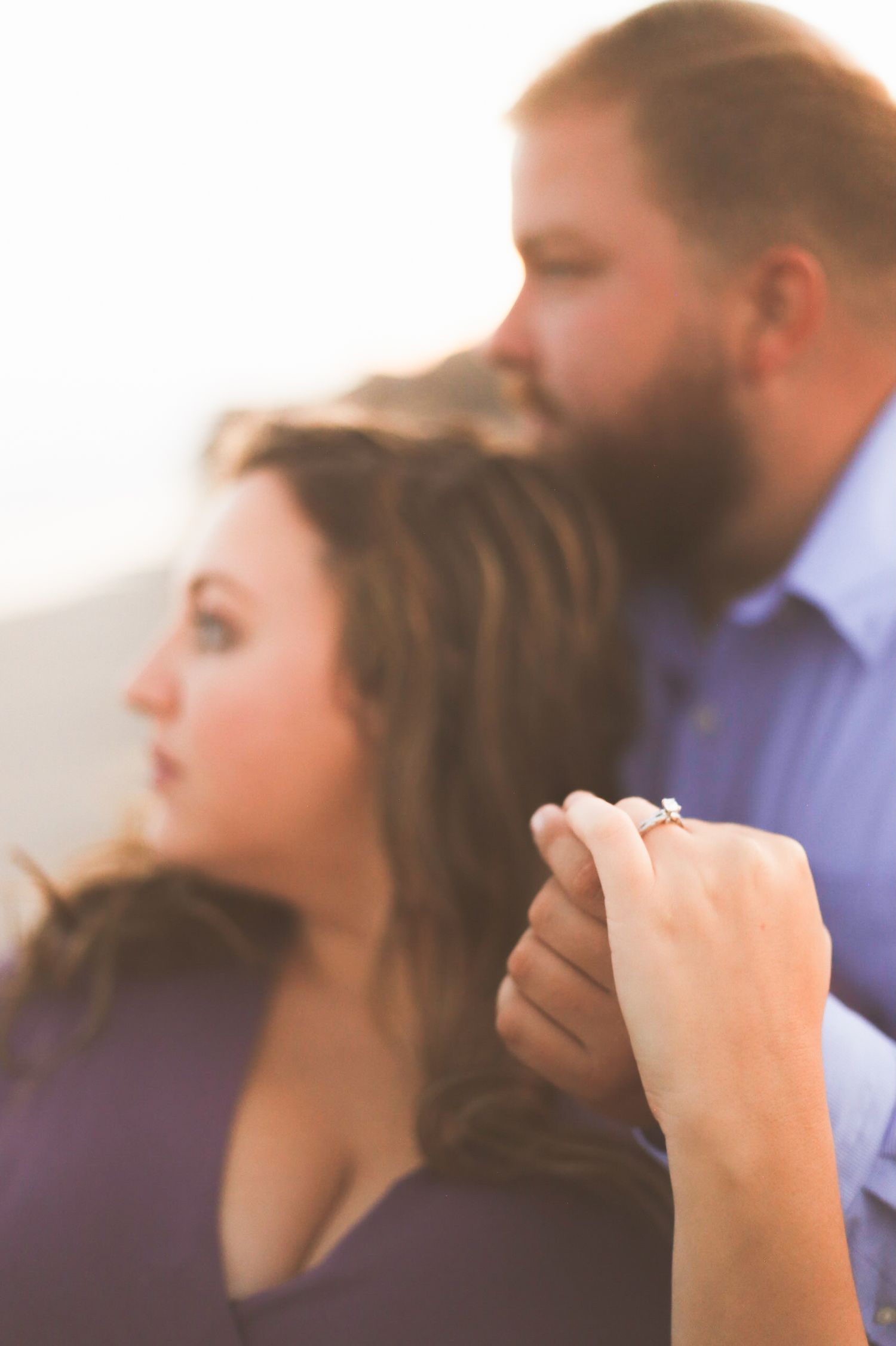 Engaged couple holding hands showing diamond ring at golden hour outdoor photo session.