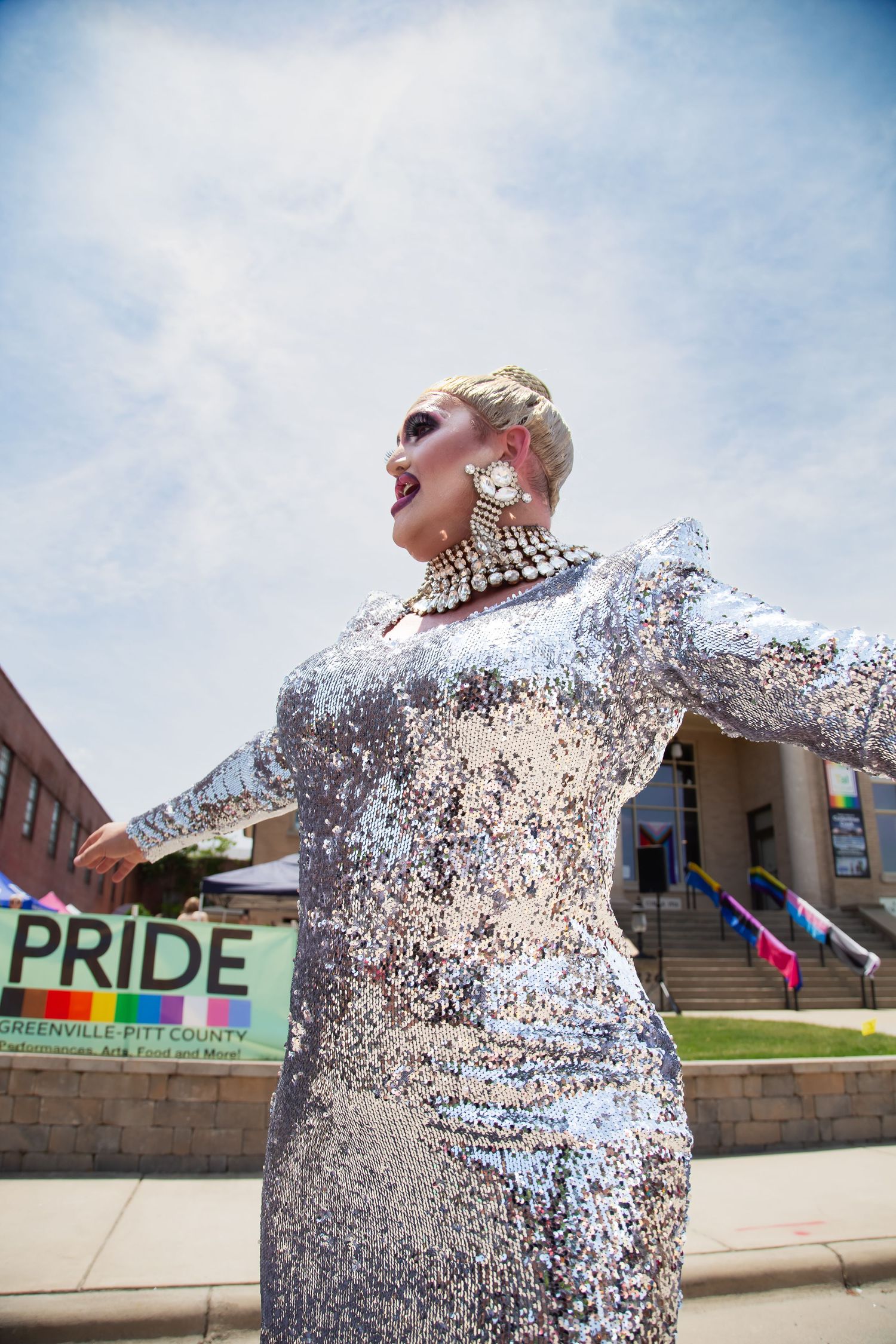 Drag performer in silver sequin gown at Greenville Pitt County Pride event under sunny sky.