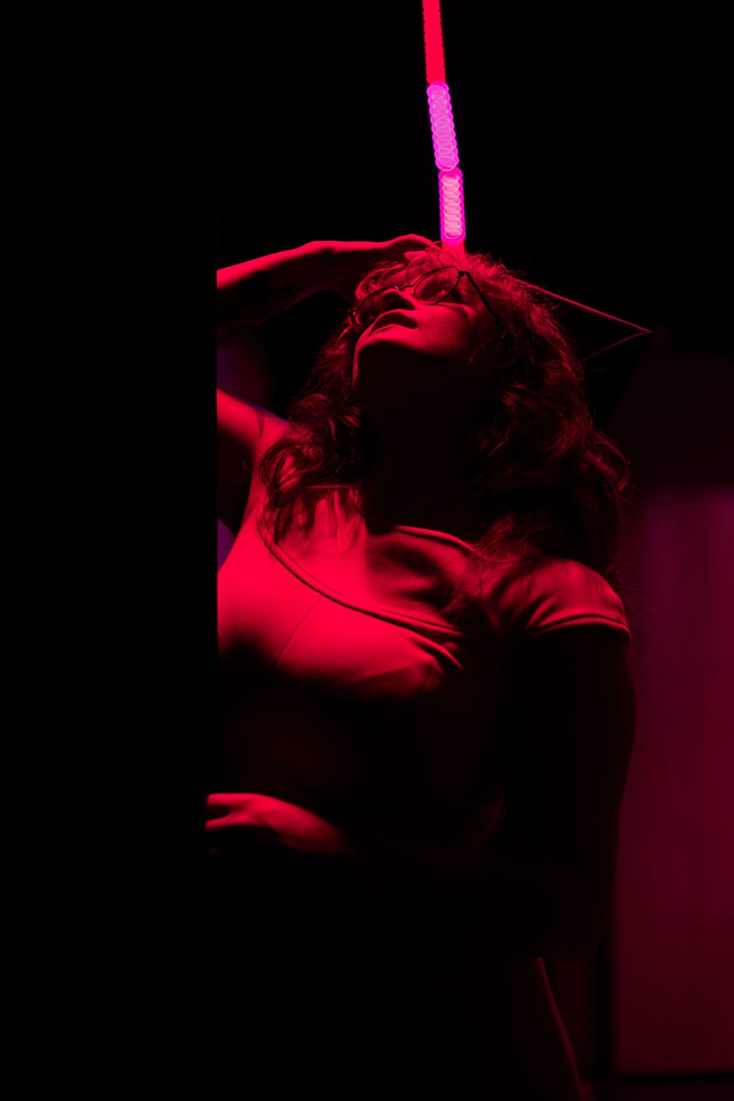 Woman posing dramatically under red neon light in dark studio setting.