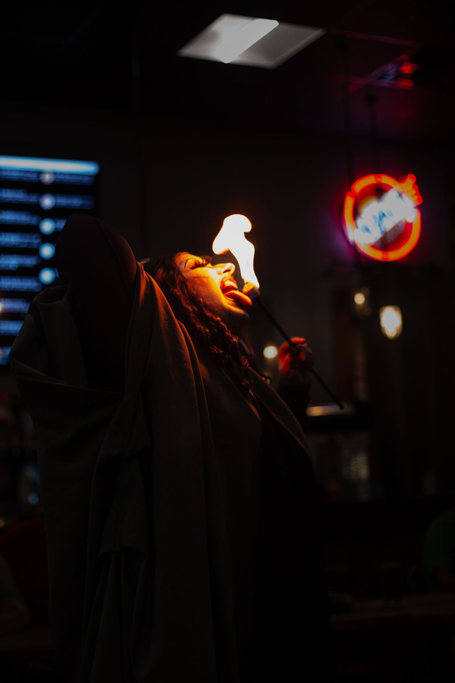 Fire performer breathing flames in a dark venue with neon signs in the background.