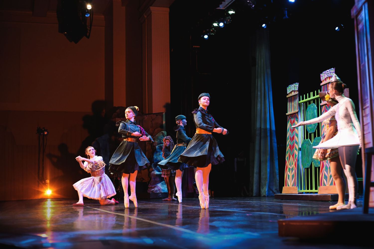 Ballet dancers perform on a theatrical stage with colorful set pieces and dramatic lighting during a live dance production.
