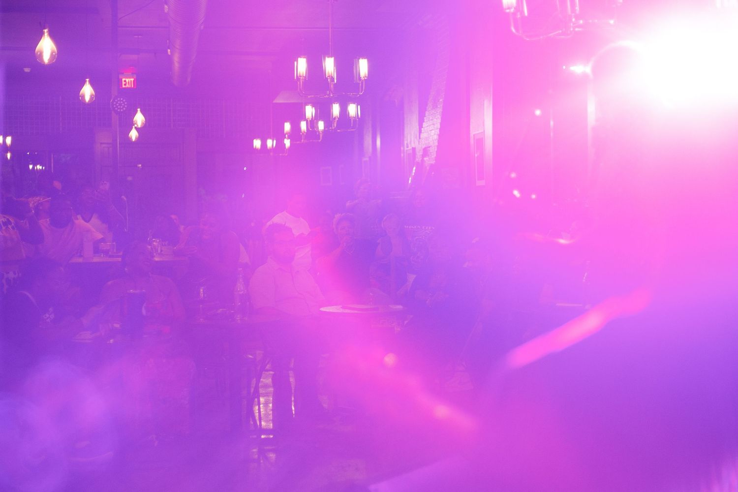 A vibrant nightclub scene bathed in pink and purple fog lights with guests seated at tables.