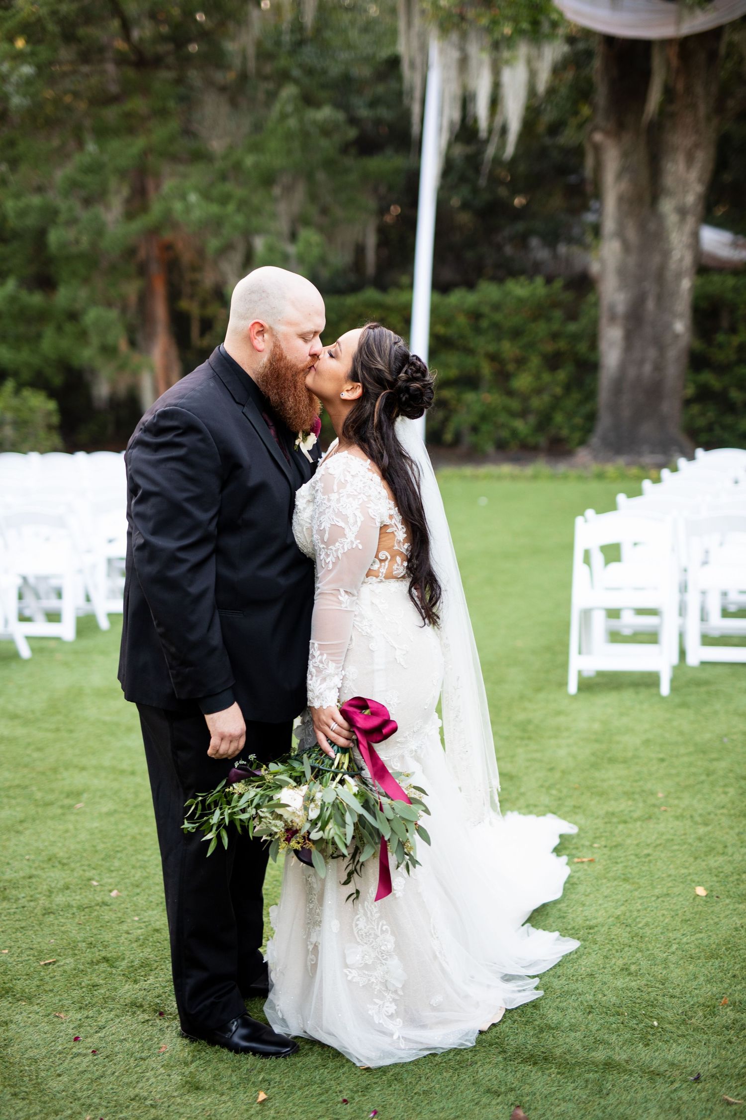 Bride and groom sharing a kiss on green lawn at outdoor wedding ceremony venue.