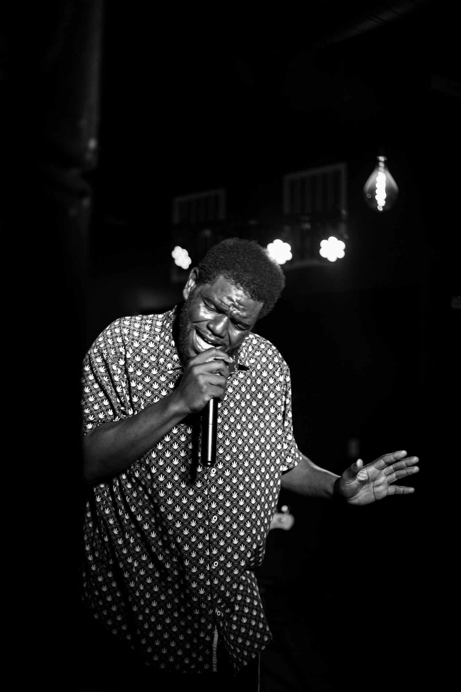 Black and white photo of a male singer performing on stage, holding a microphone with stage lights behind him.