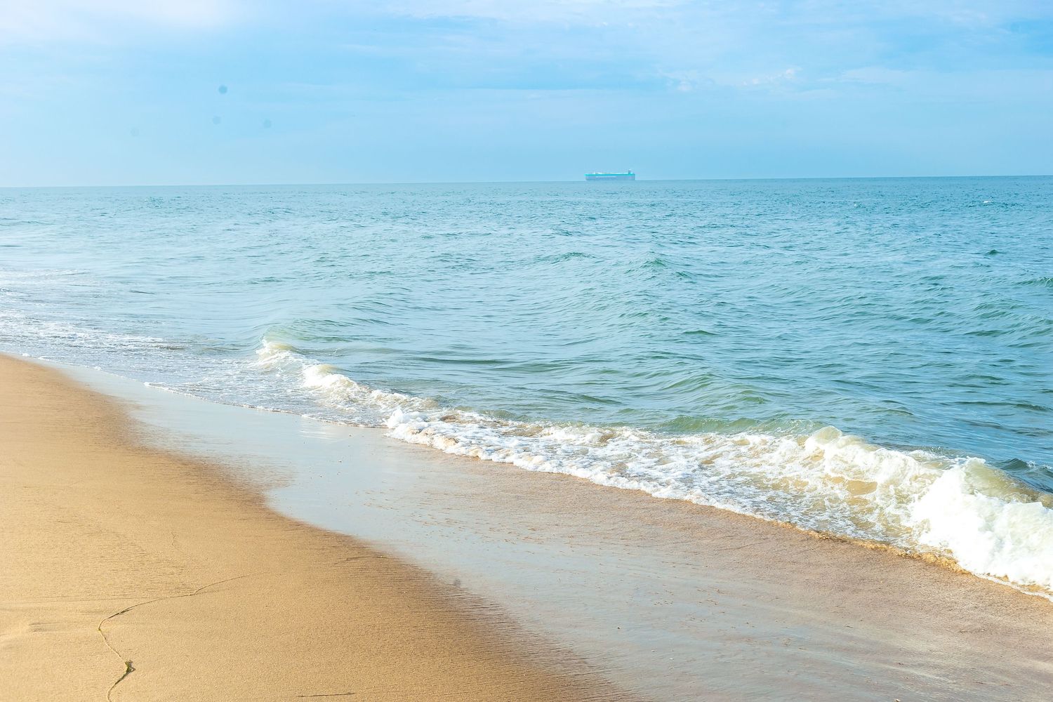 Calm ocean waves gently washing onto a sandy beach under a clear blue sky.