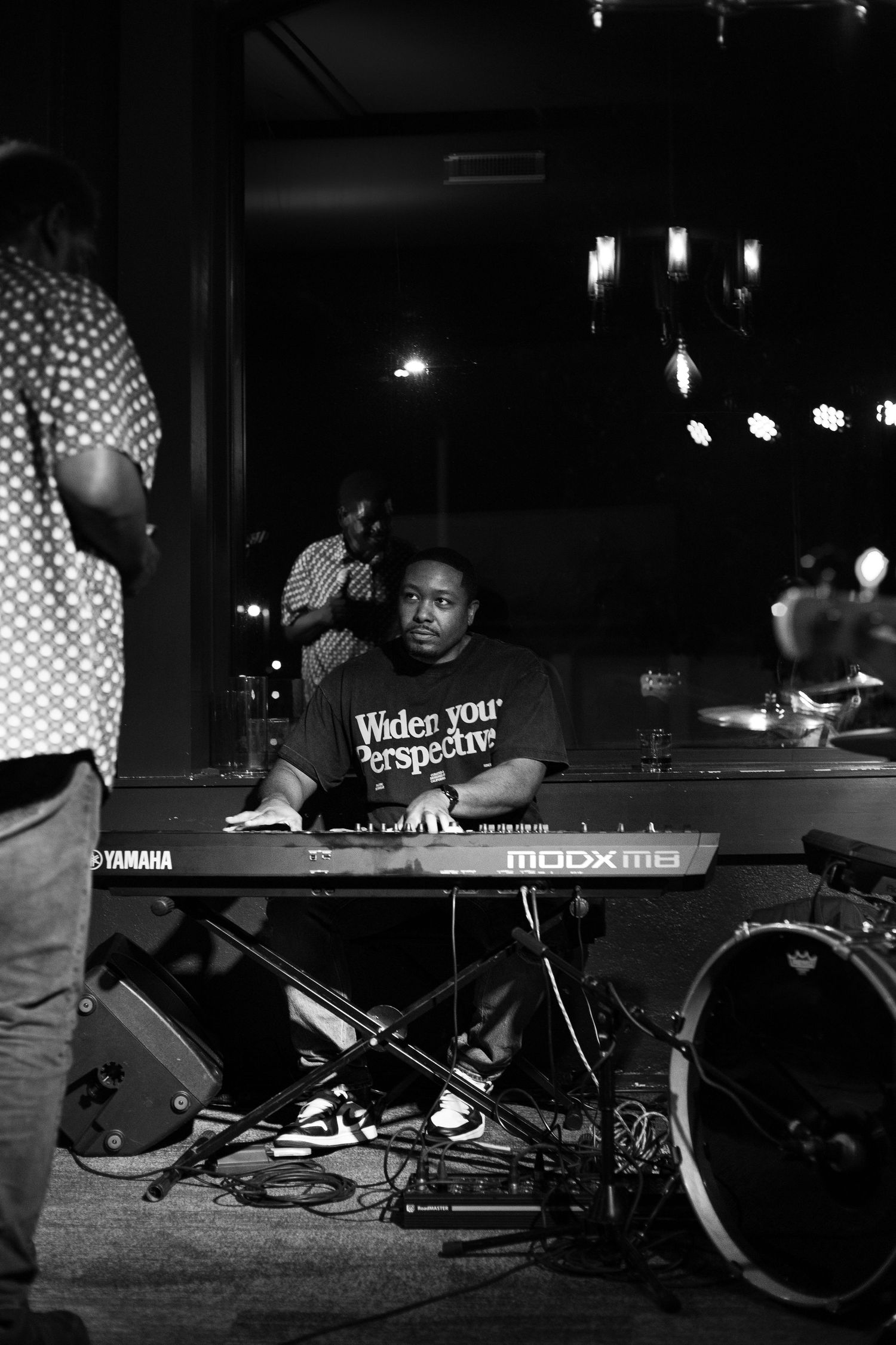 Black and white photo of a musician playing a Yamaha MODX8 keyboard on stage at a live music venue.