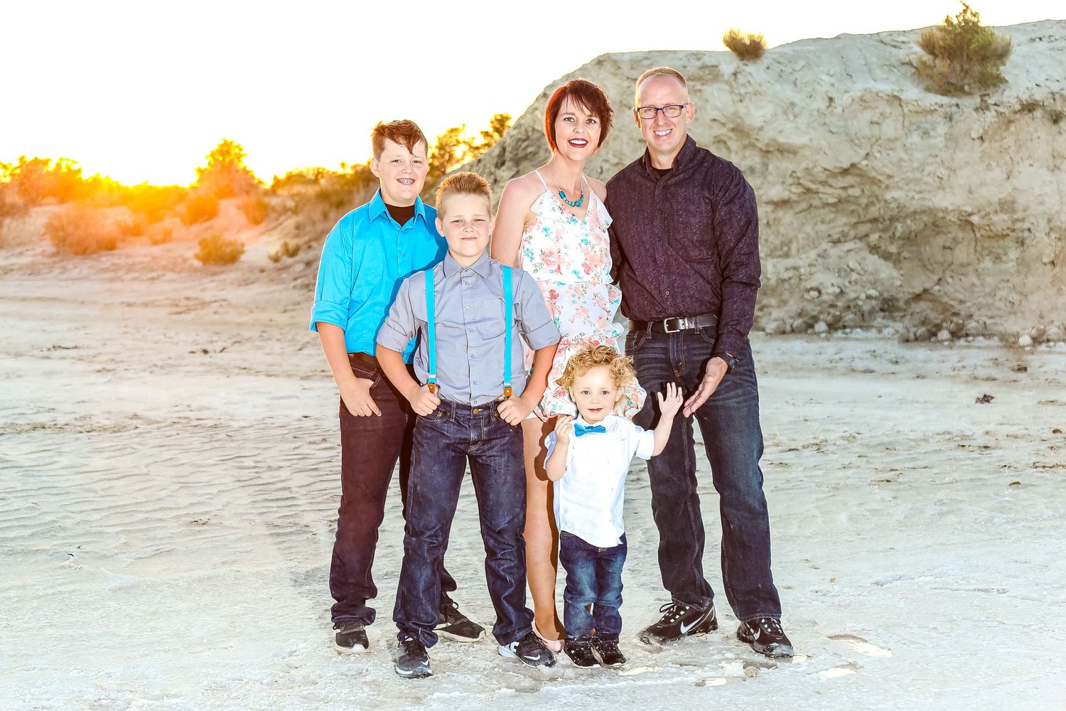 Family of five posing together on a sandy beach at golden hour sunset with warm glowing light.