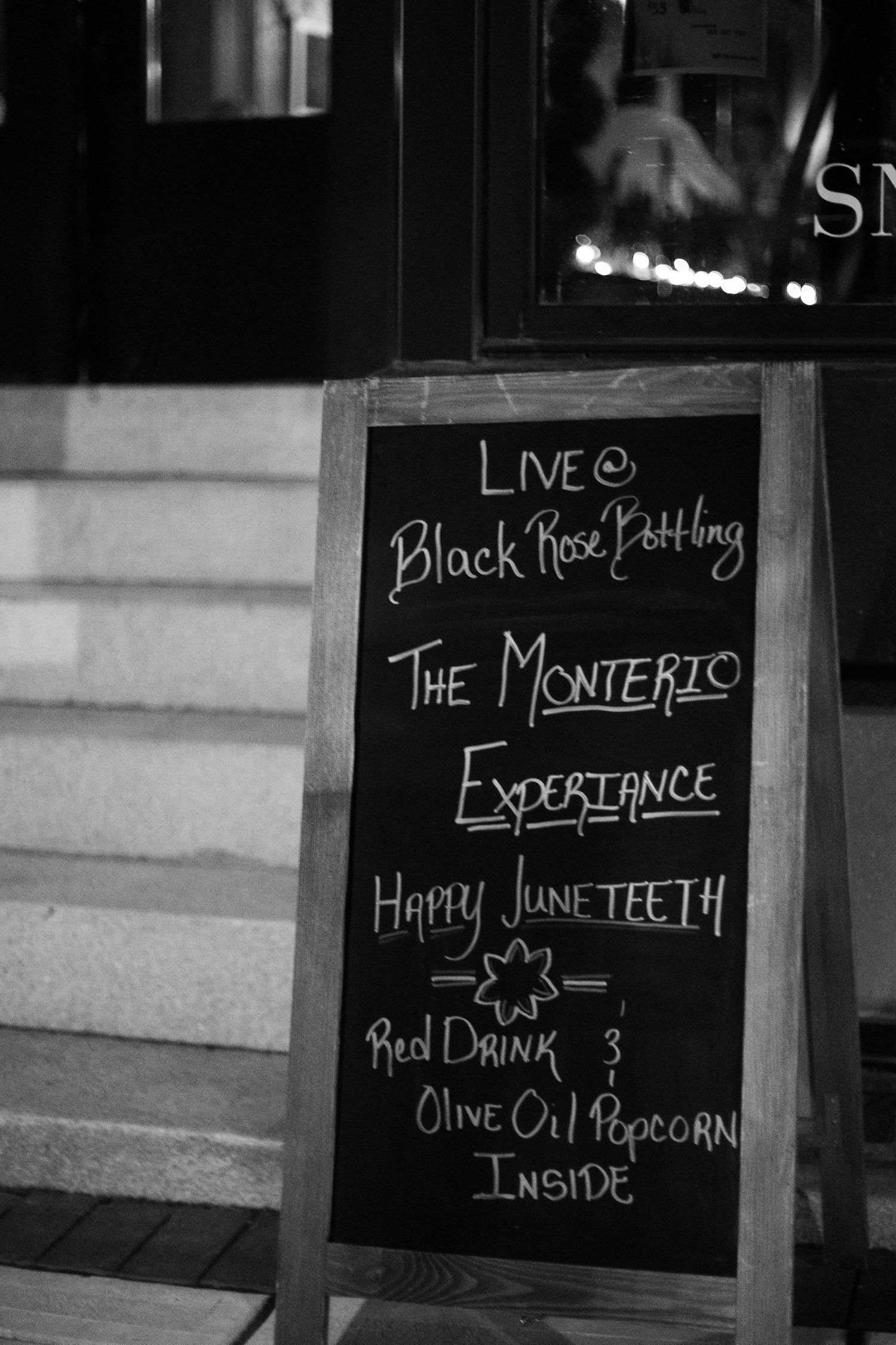 Black chalkboard sign advertising live music at Black Rose, The Monterio Experience, Happy Juneteenth, red drink $3, popcorn inside.