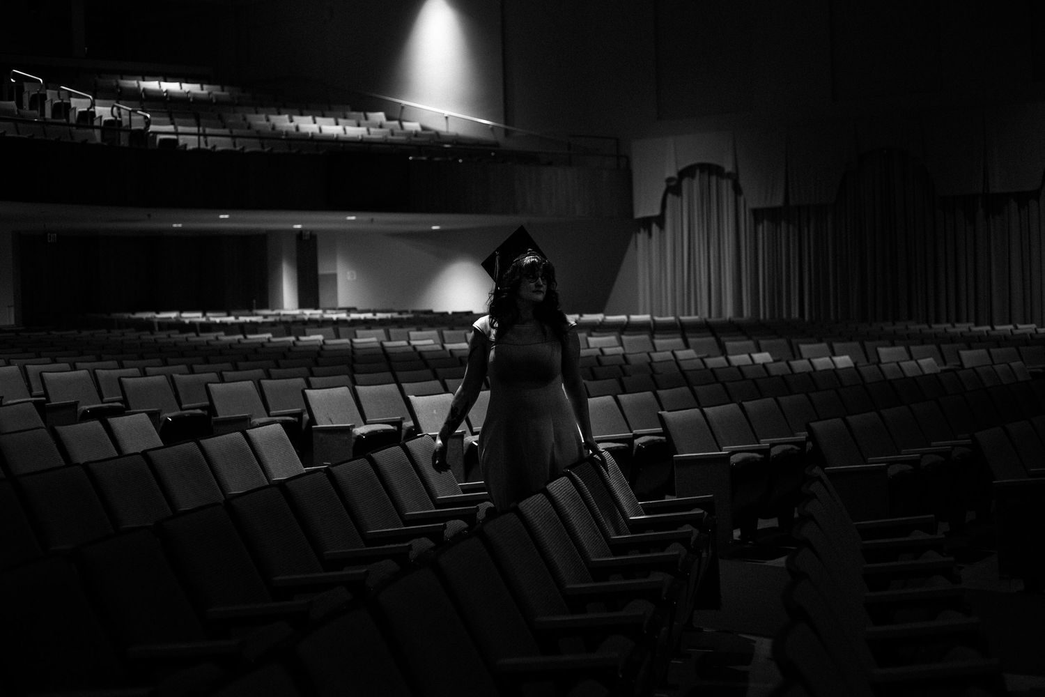 A lone woman in a dress stands in an empty theater auditorium, captured in dramatic black and white photography.