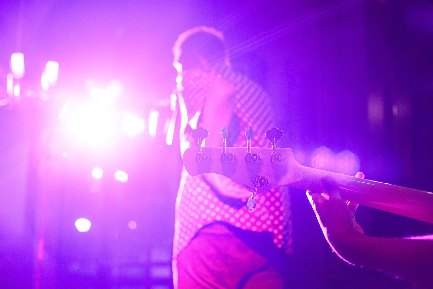 Guitarist performing on stage bathed in vibrant purple and pink lights during a live concert.