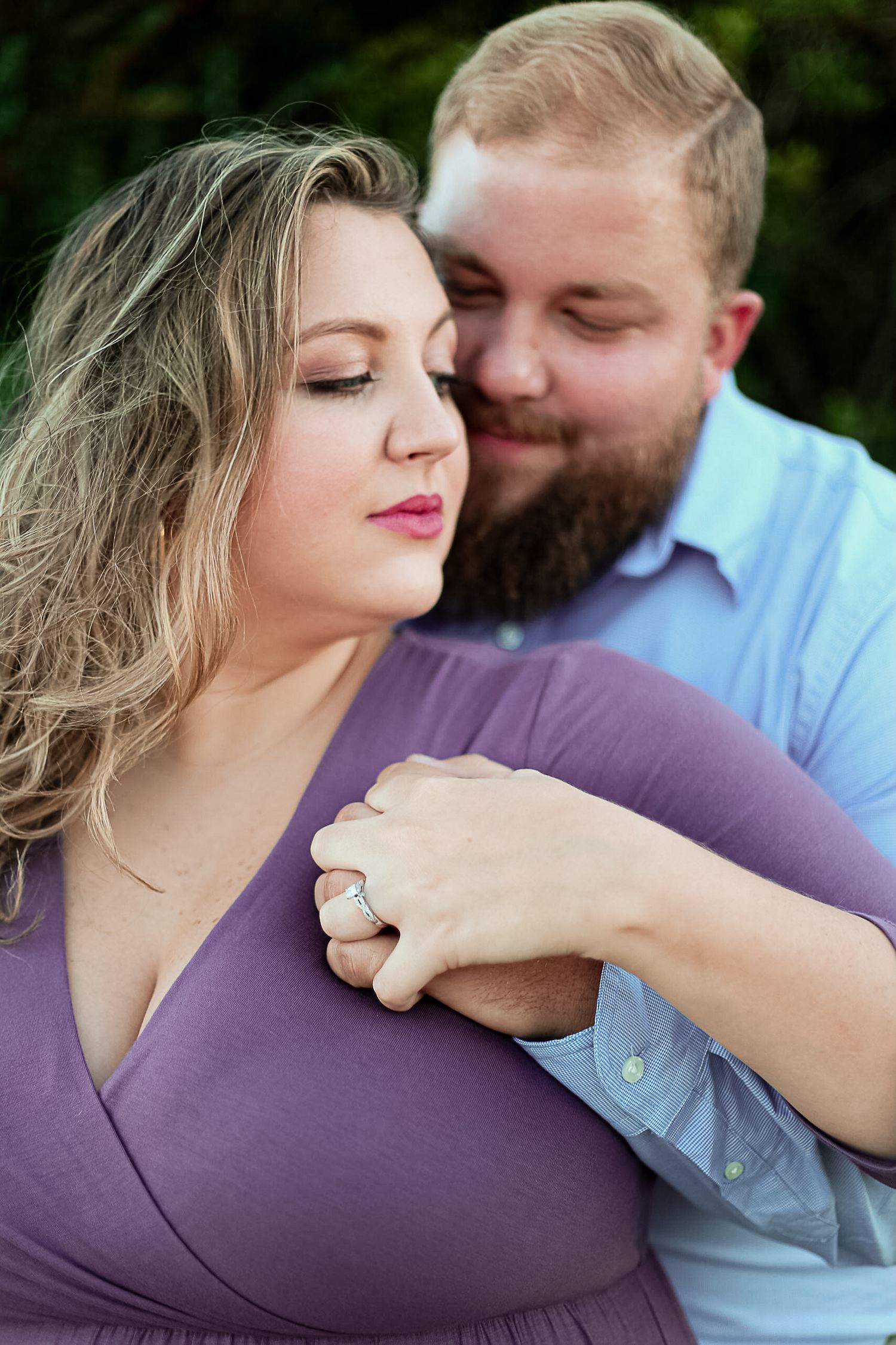 Couple in romantic embrace, woman in purple dress with engagement ring, man in blue shirt with beard.
