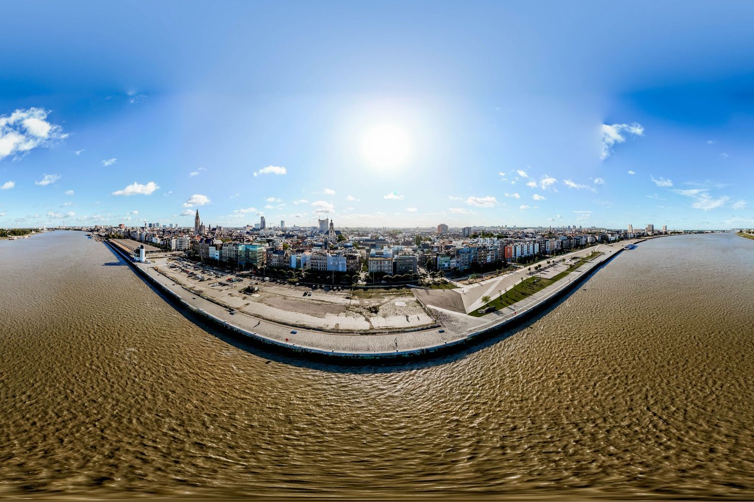 Aerial panoramic view of a coastal city skyline along a wide river under a bright sunny sky.