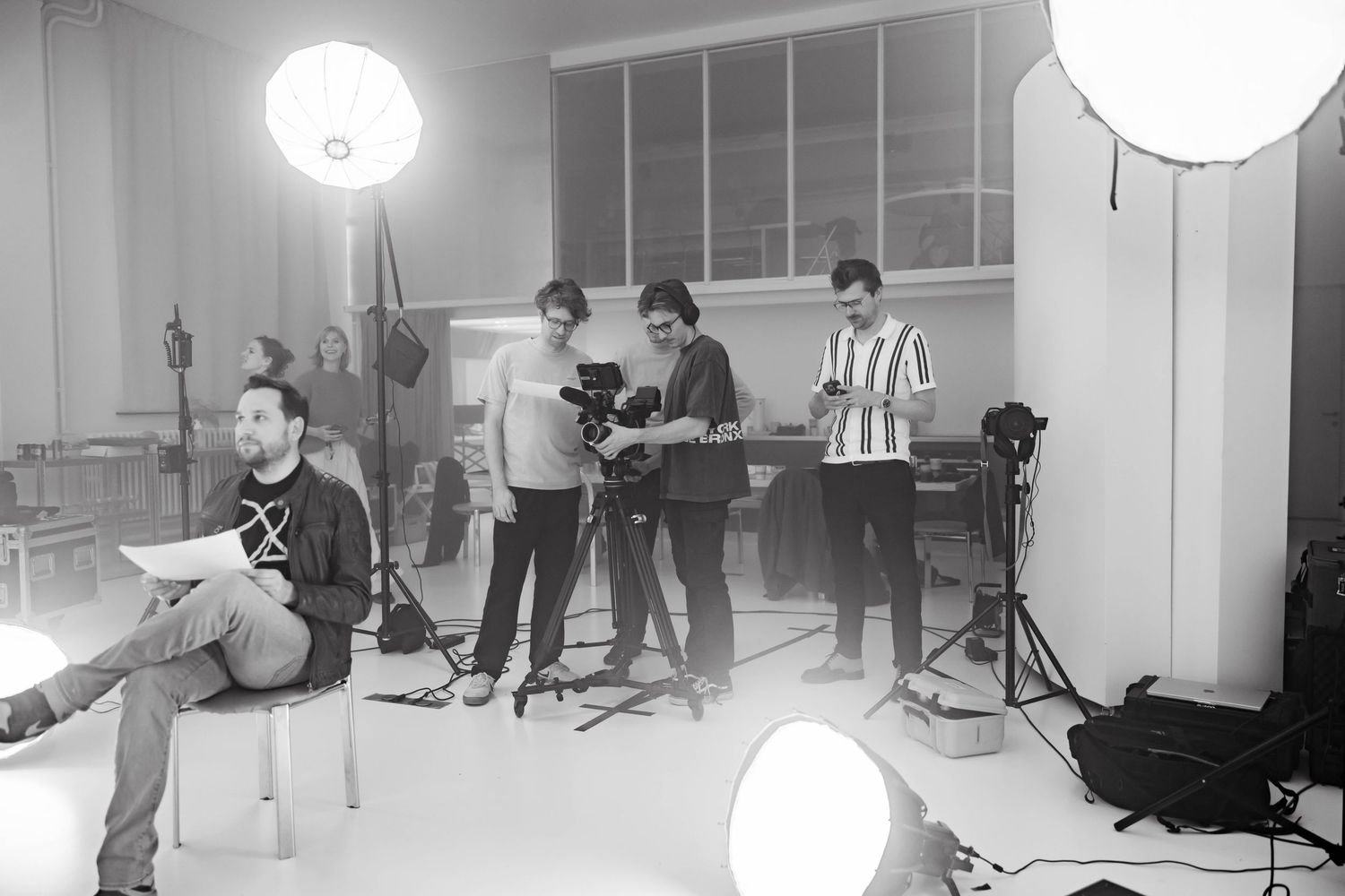 Black and white photo of a film crew shooting a video in a bright studio with professional lighting equipment.