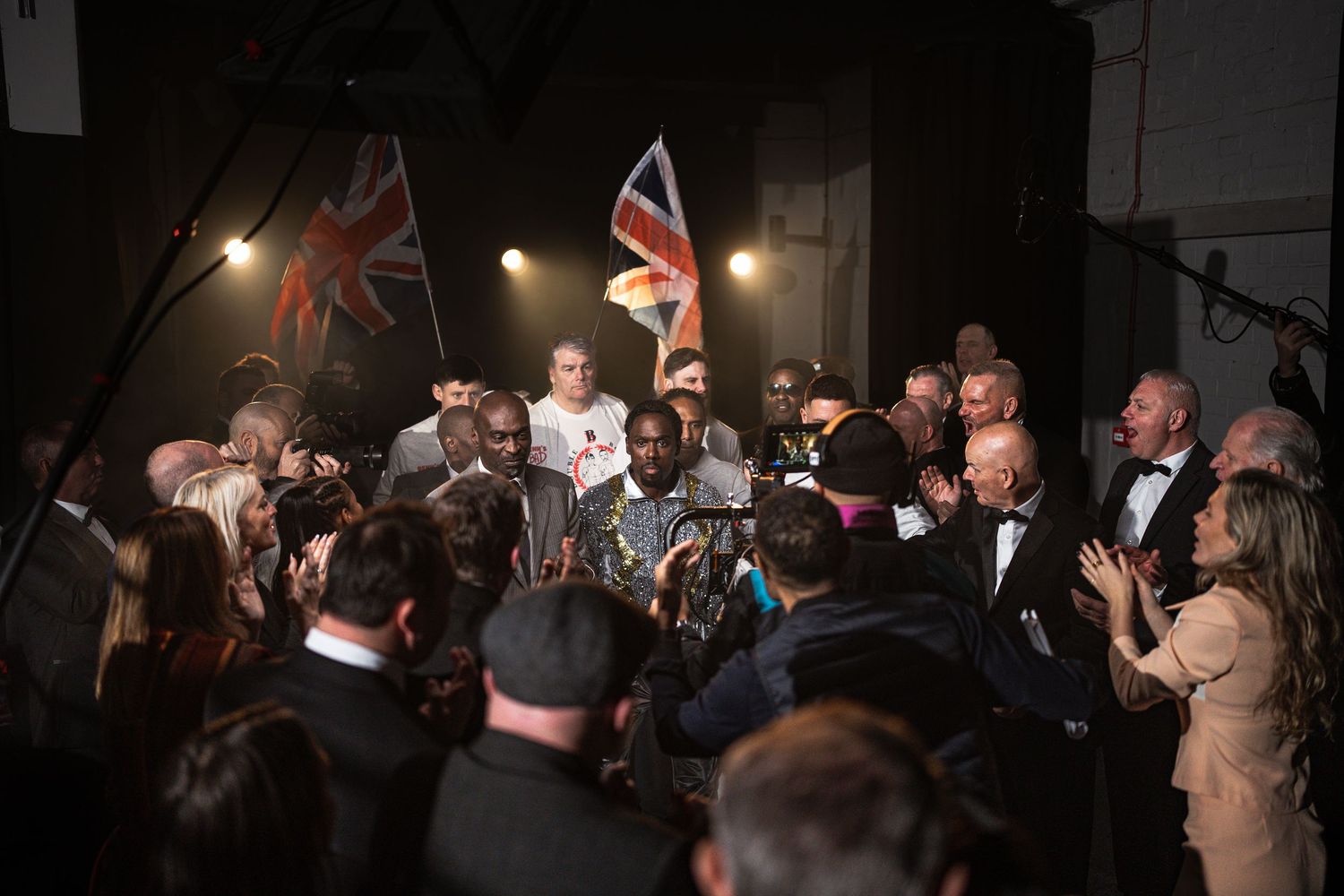 Boxer surrounded by crowd with British flags in dramatic backstage boxing event.
