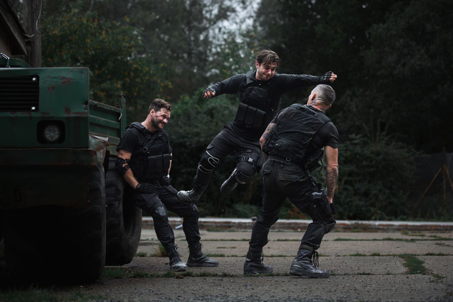 Three men in black tactical gear fighting near military vehicle outdoors.
