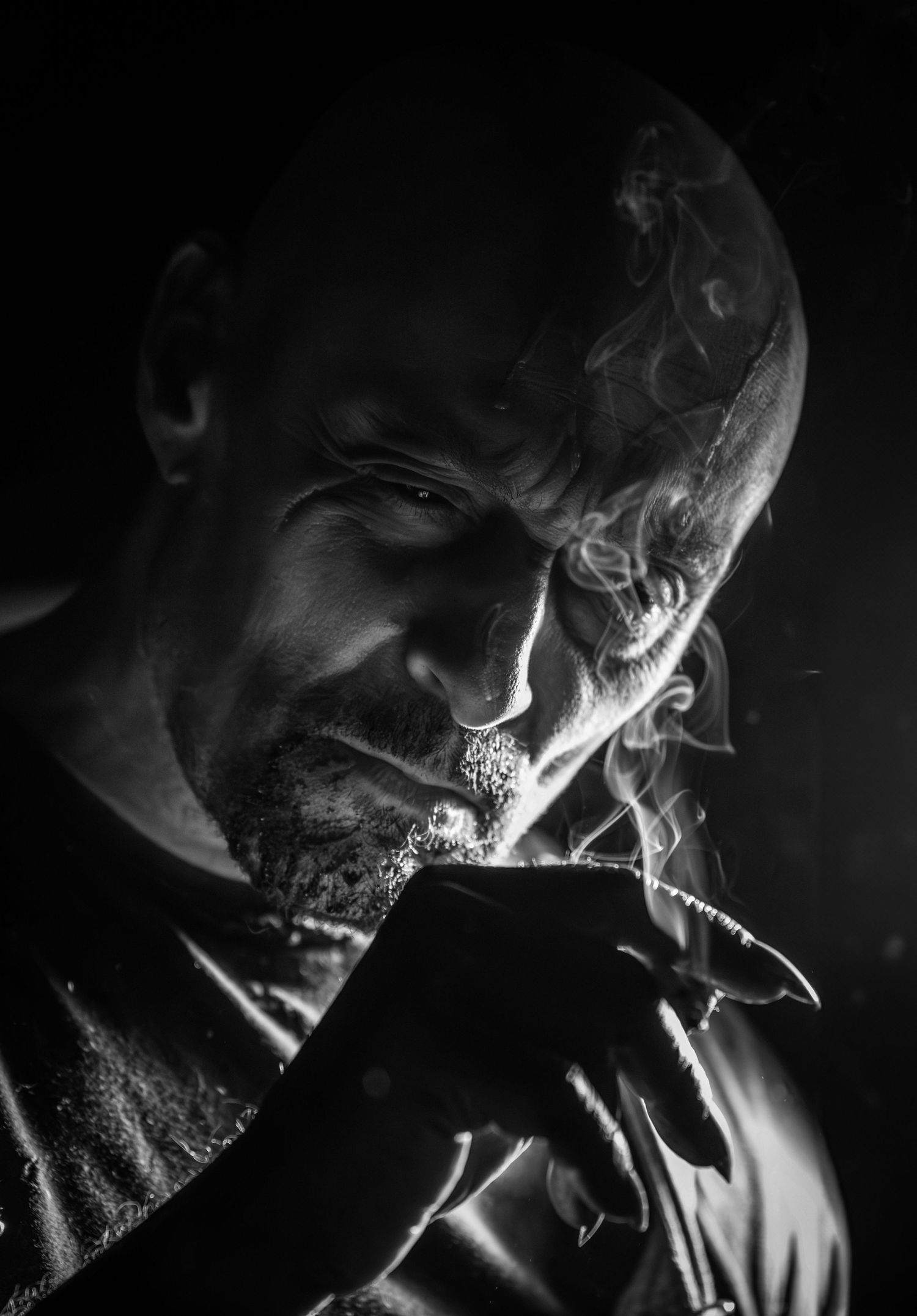 Black and white portrait of a man smoking in dramatic low-key lighting with smoke swirling above.