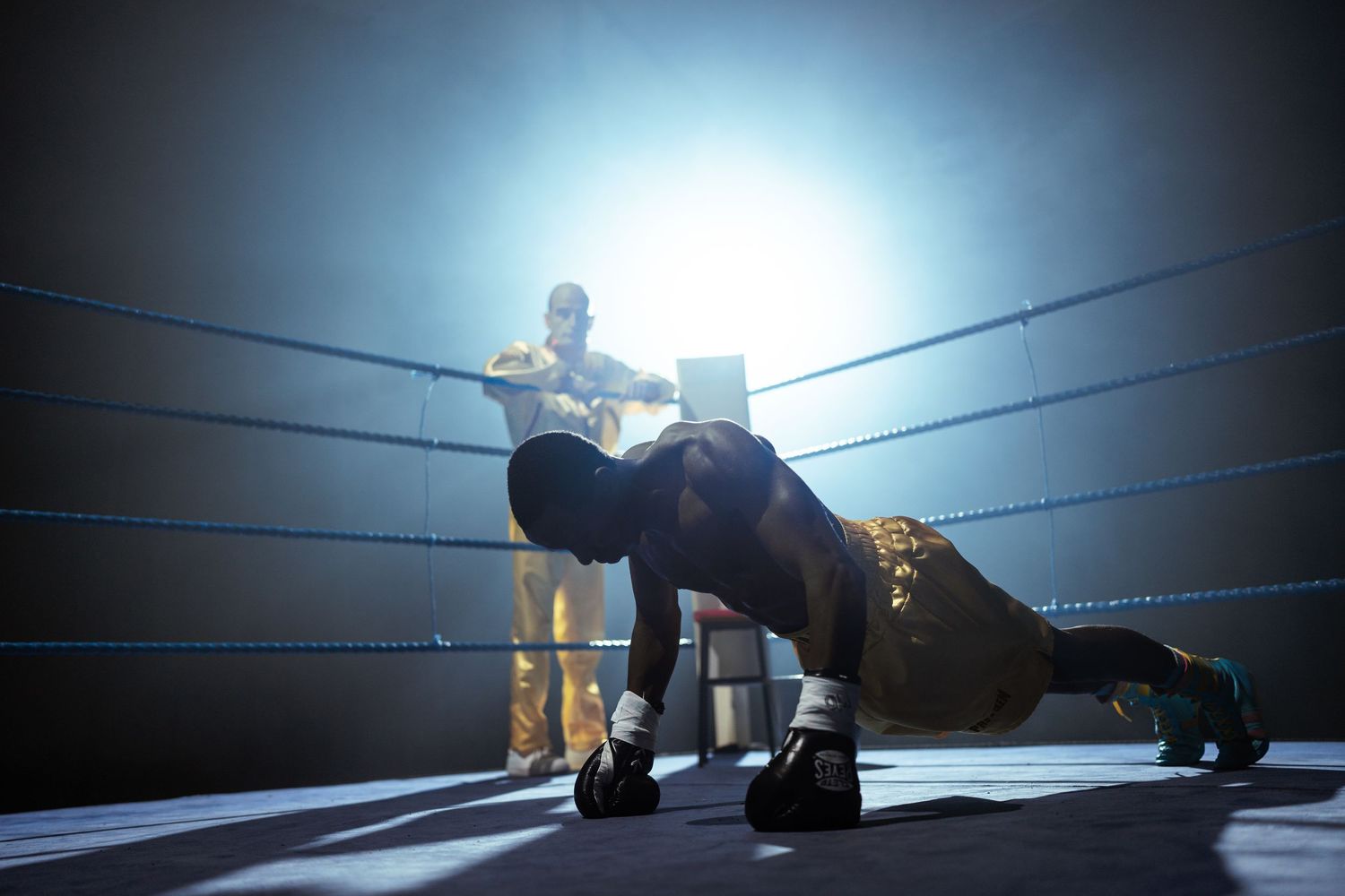 Boxer doing push-ups in boxing ring corner during professional fight training session.