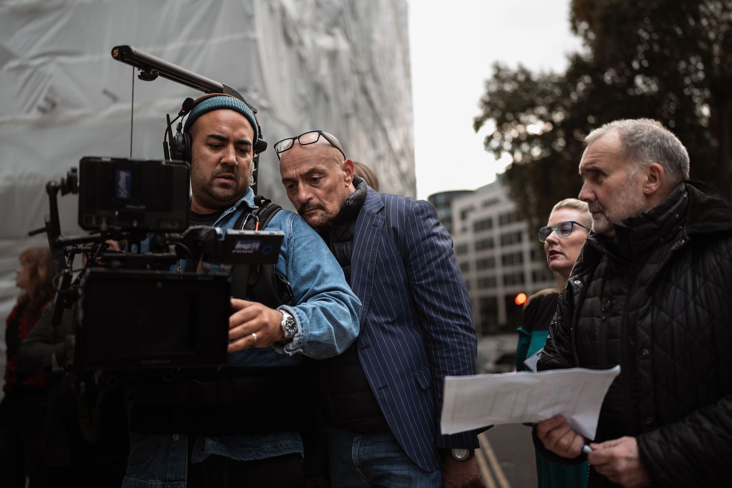 Film crew reviewing camera footage on outdoor movie set in urban location.