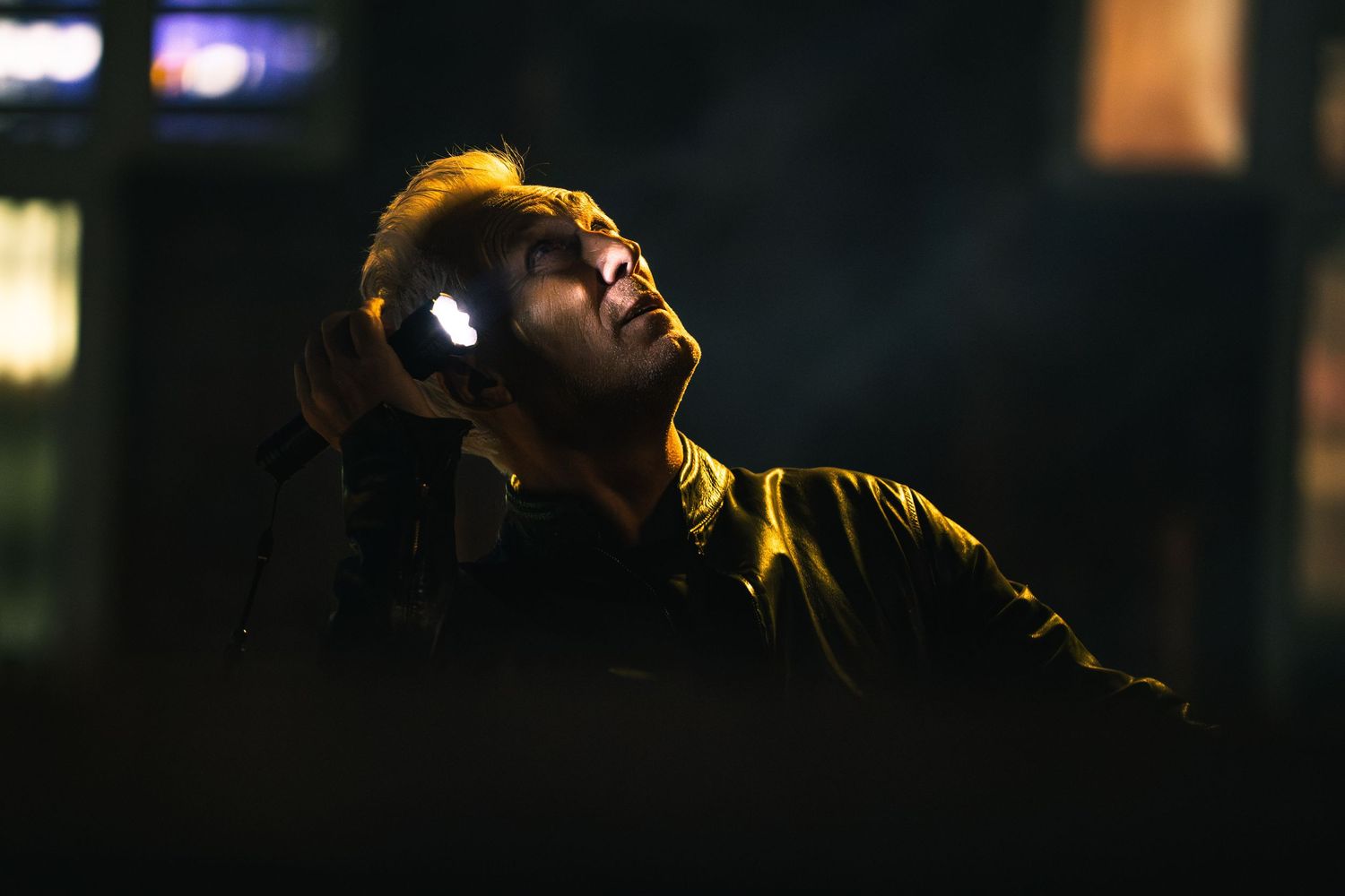 A man wearing headphones looks upward dramatically against a dark urban night background.