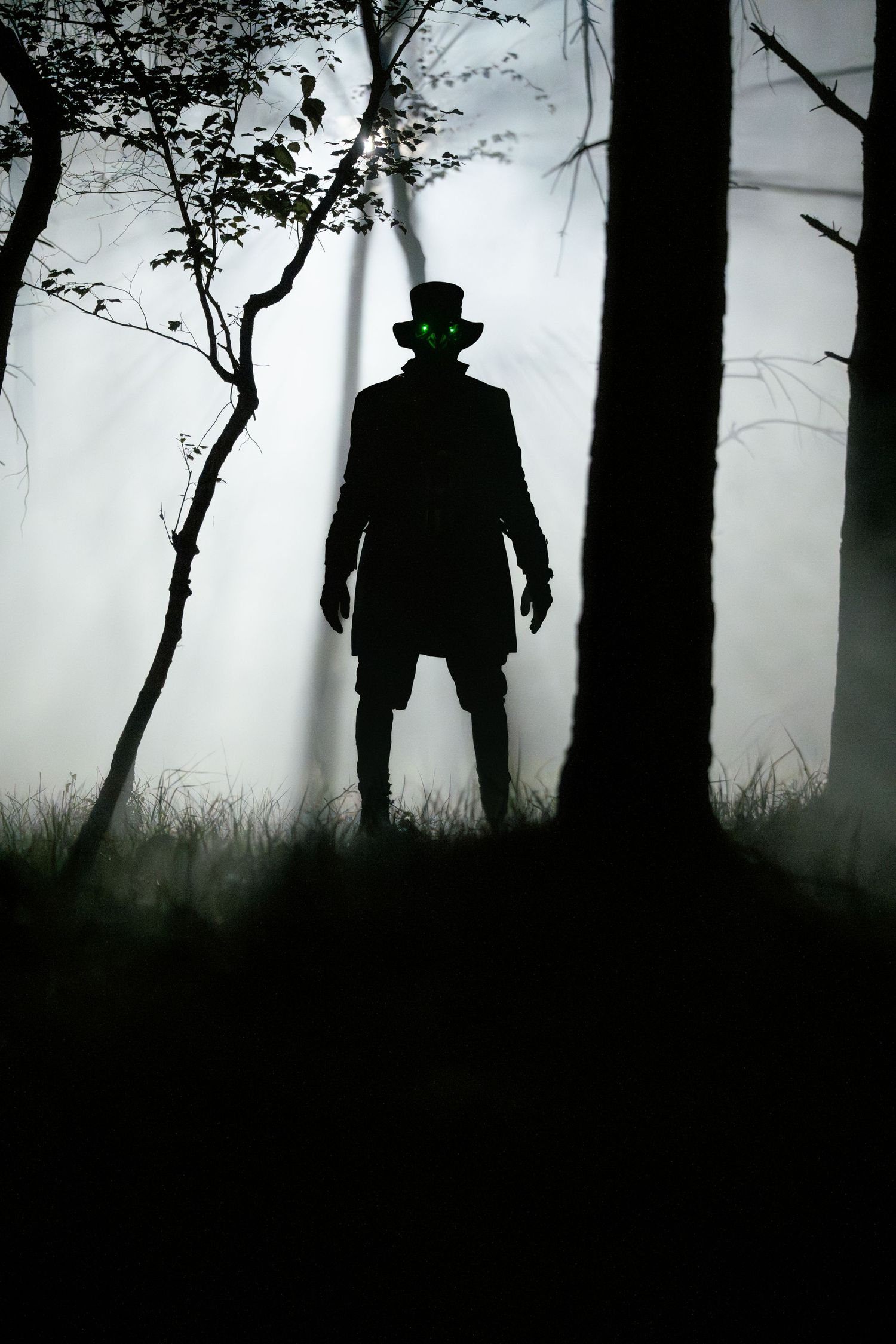 A mysterious silhouette of a figure in a top hat stands in a misty forest at night.
